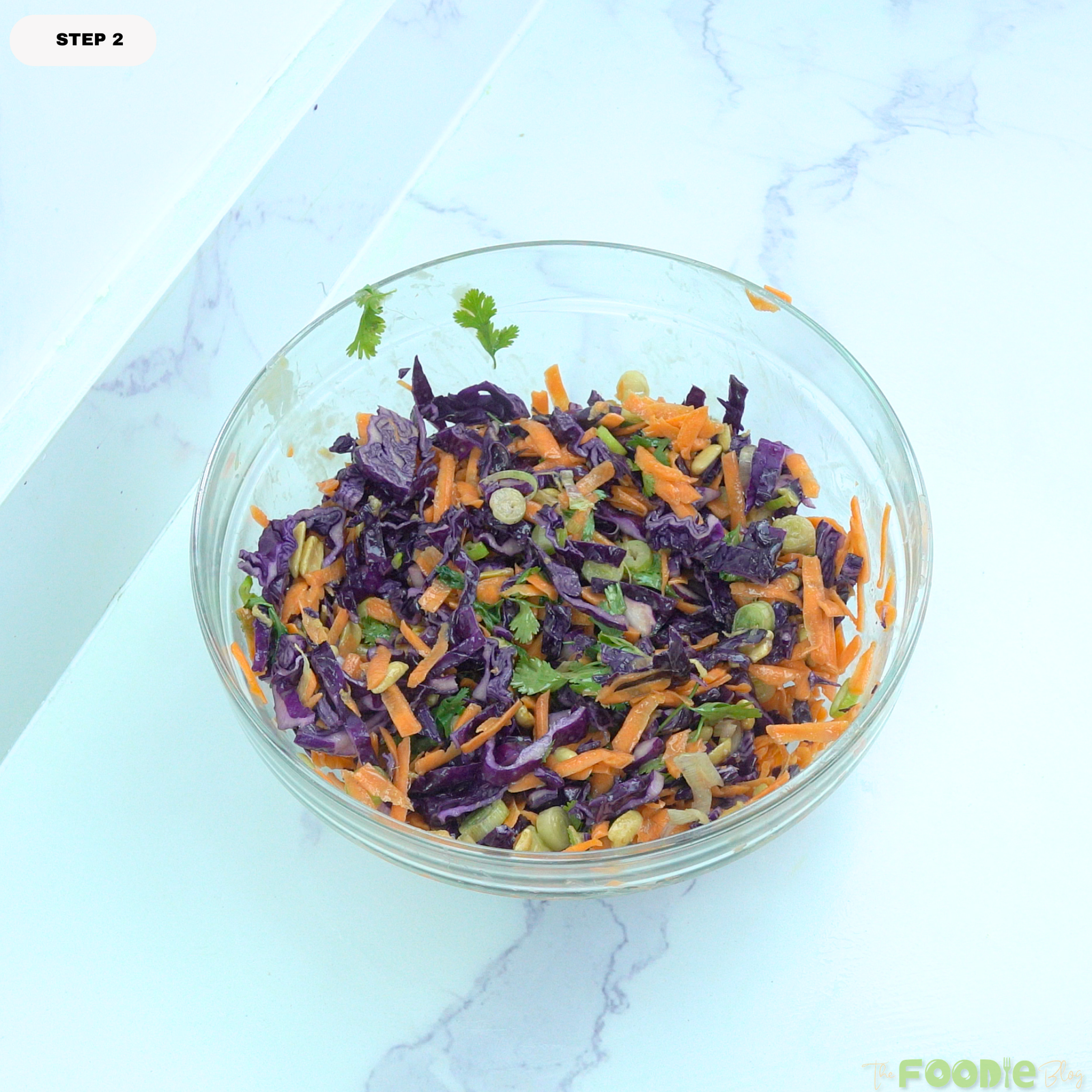 Purple cabbage, carrots, green onions, cilantro, and peanuts tossed together in a glass bowl with sesame ginger dressing.