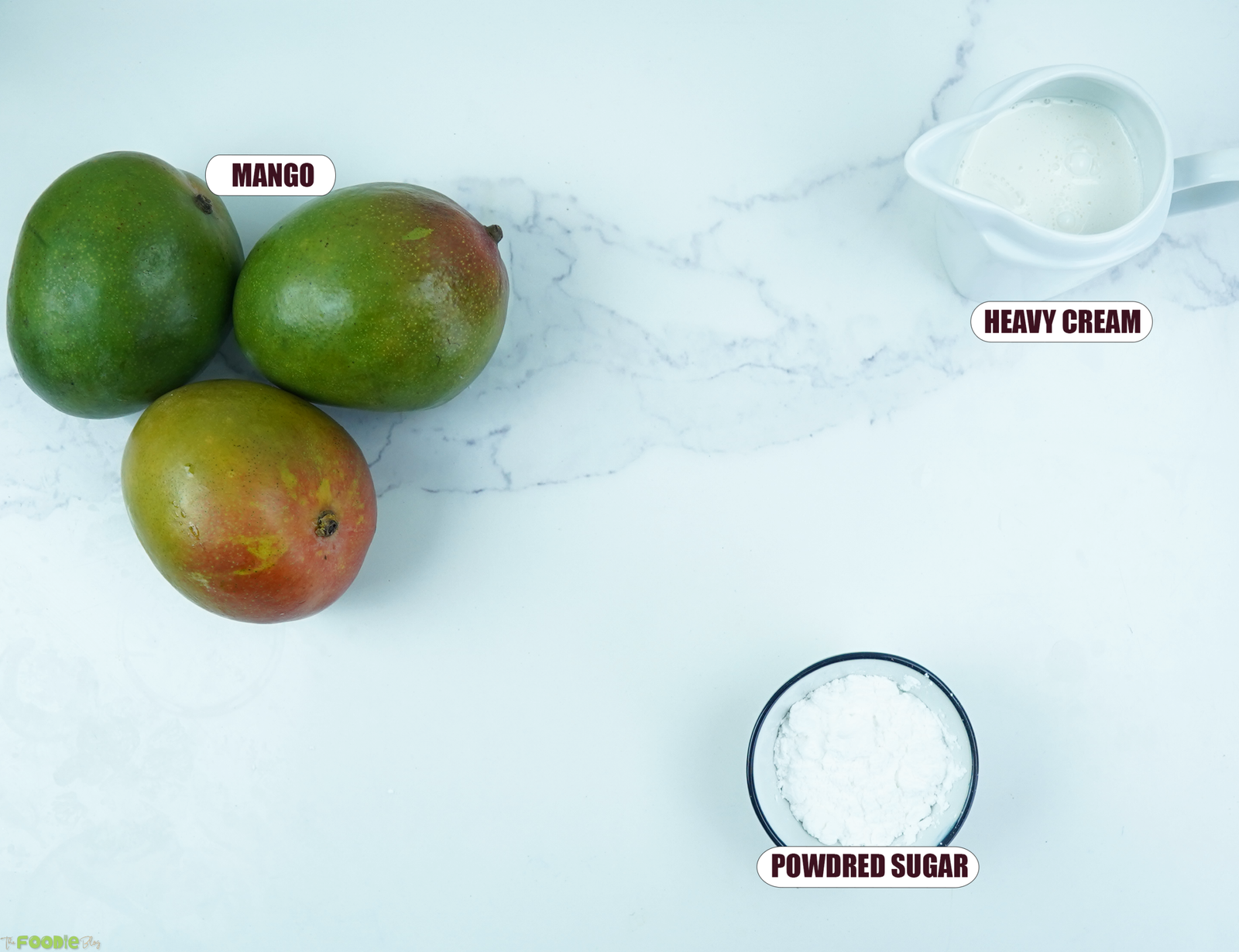 Ingredients for easy mango mousse with fresh mangoes, heavy cream, and powdered sugar on a marble surfac