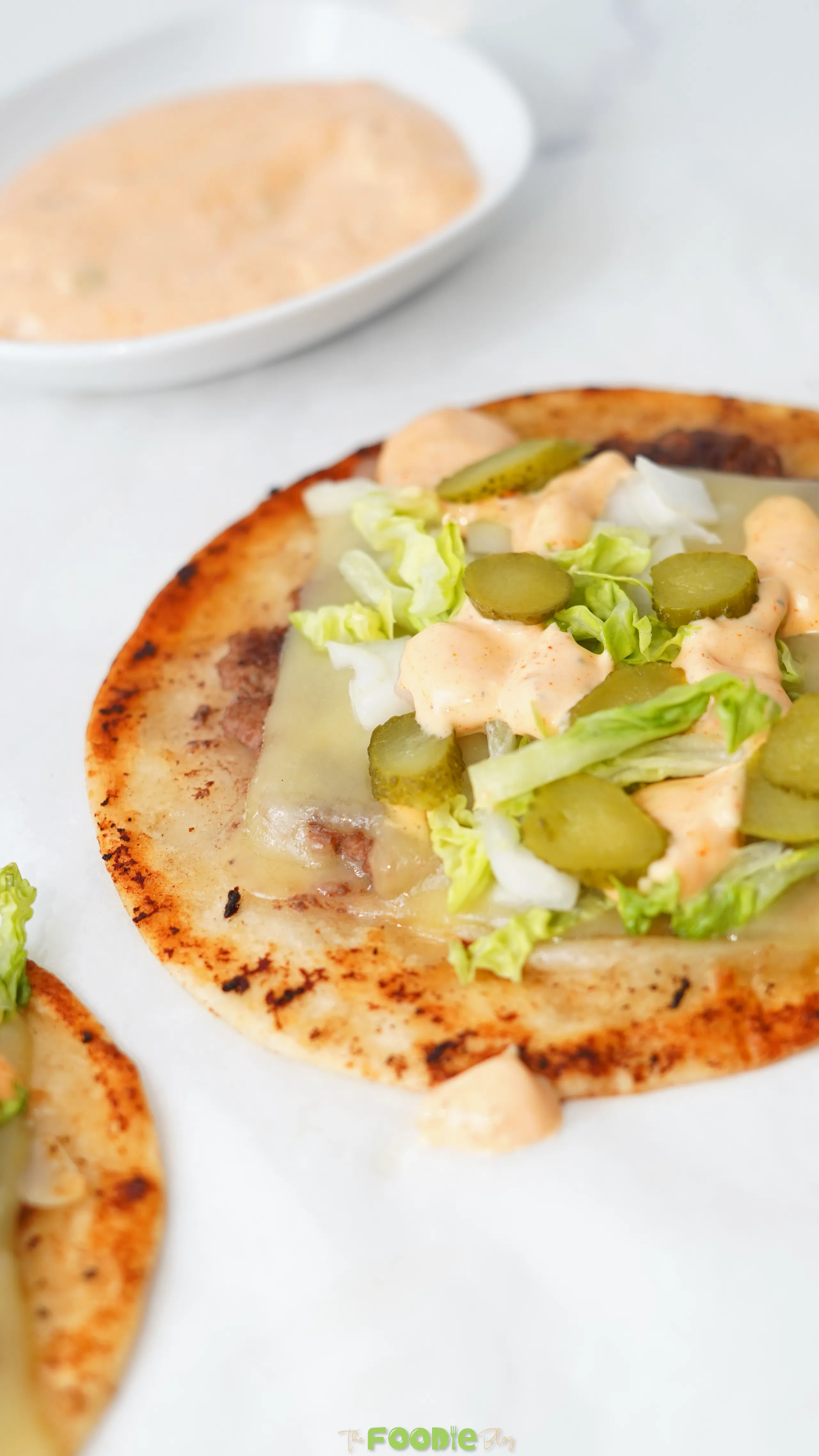 Smash burger taco topped with melted cheese, shredded lettuce, chopped onion, dill pickles, and burger sauce.