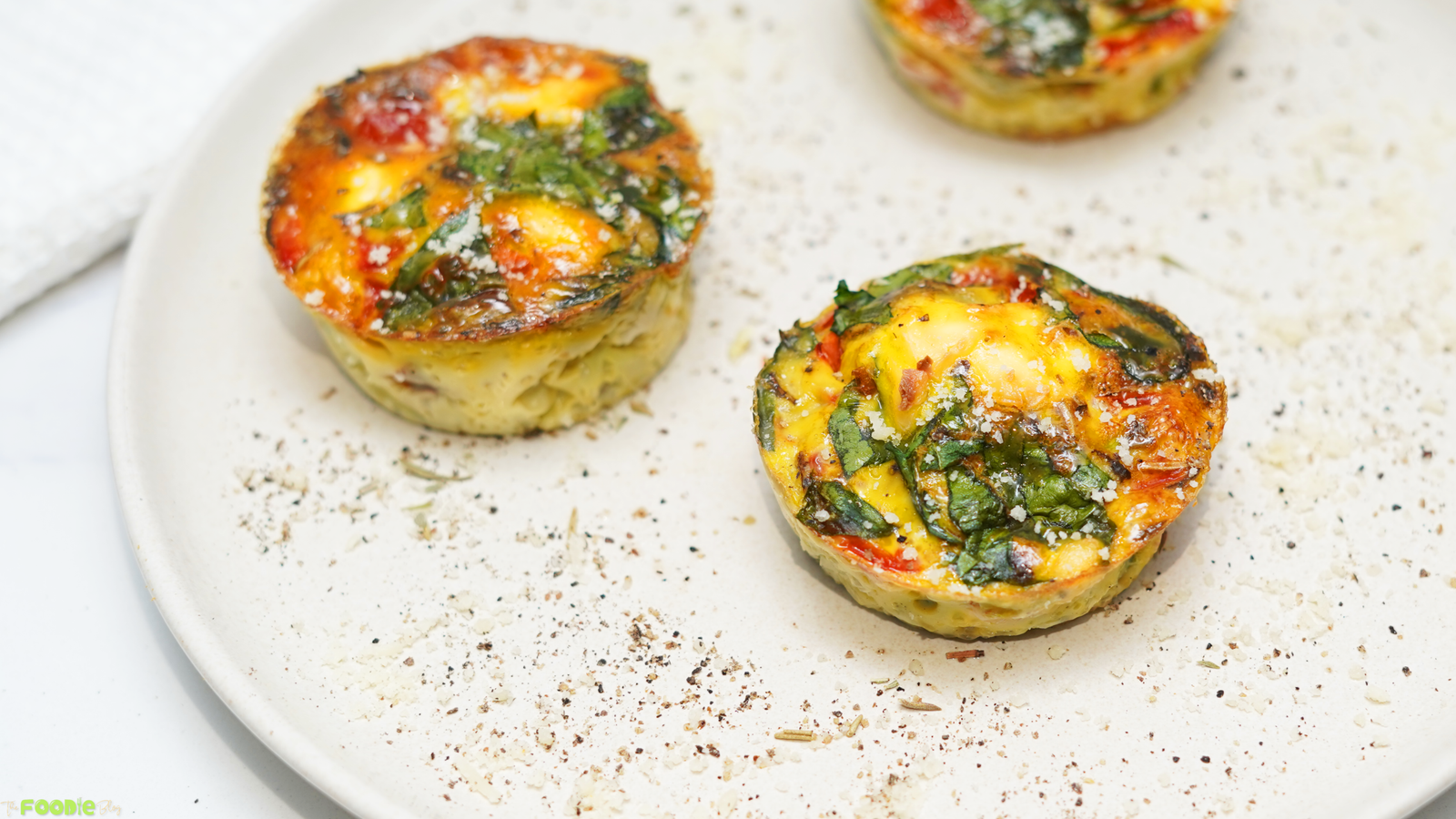 Two baked egg muffins with spinach, tomatoes, peppers, herbs, and feta served on a large plate.