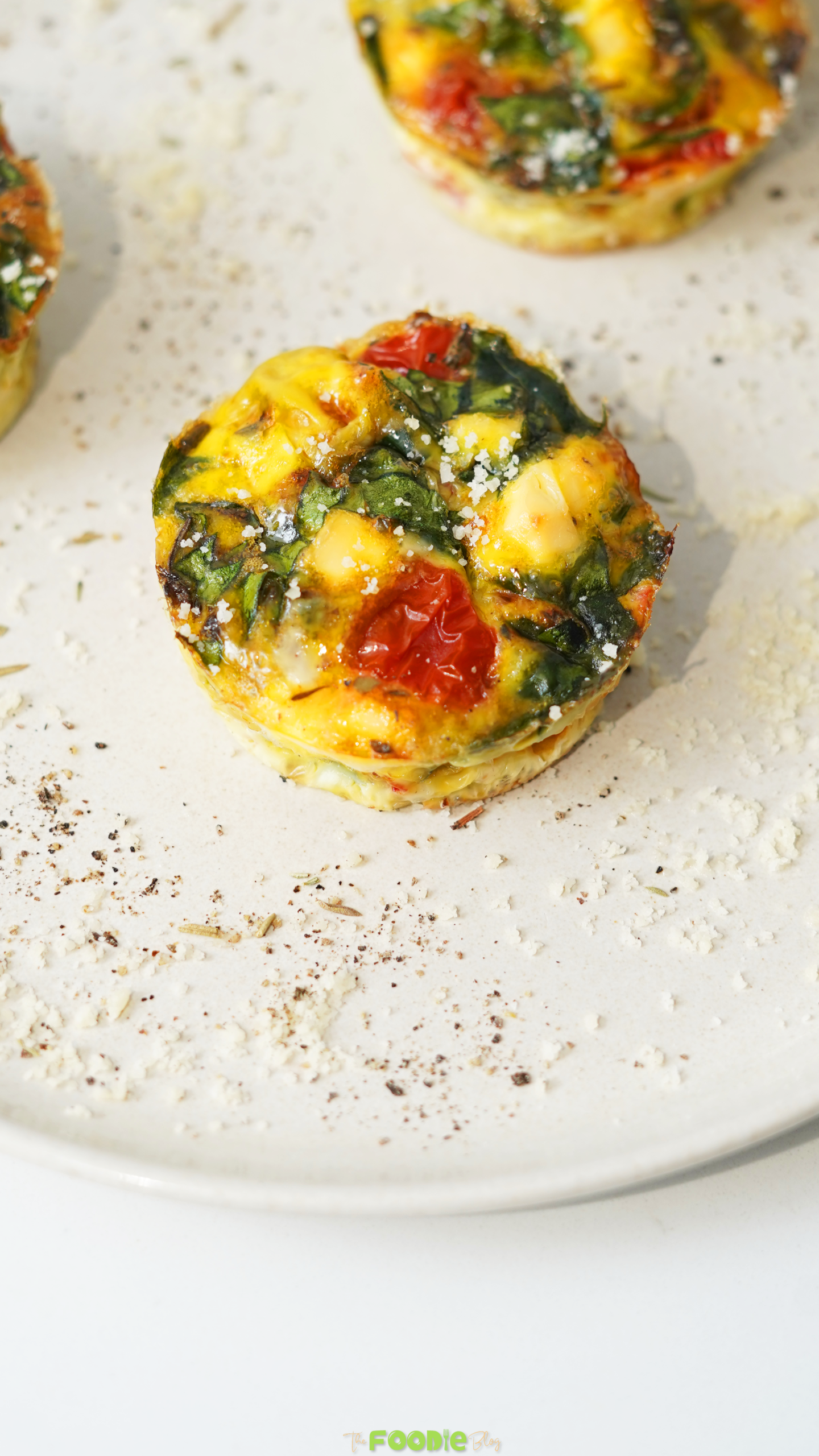 Baked egg muffin with spinach, tomatoes, bell peppers, and feta served on a white plate.