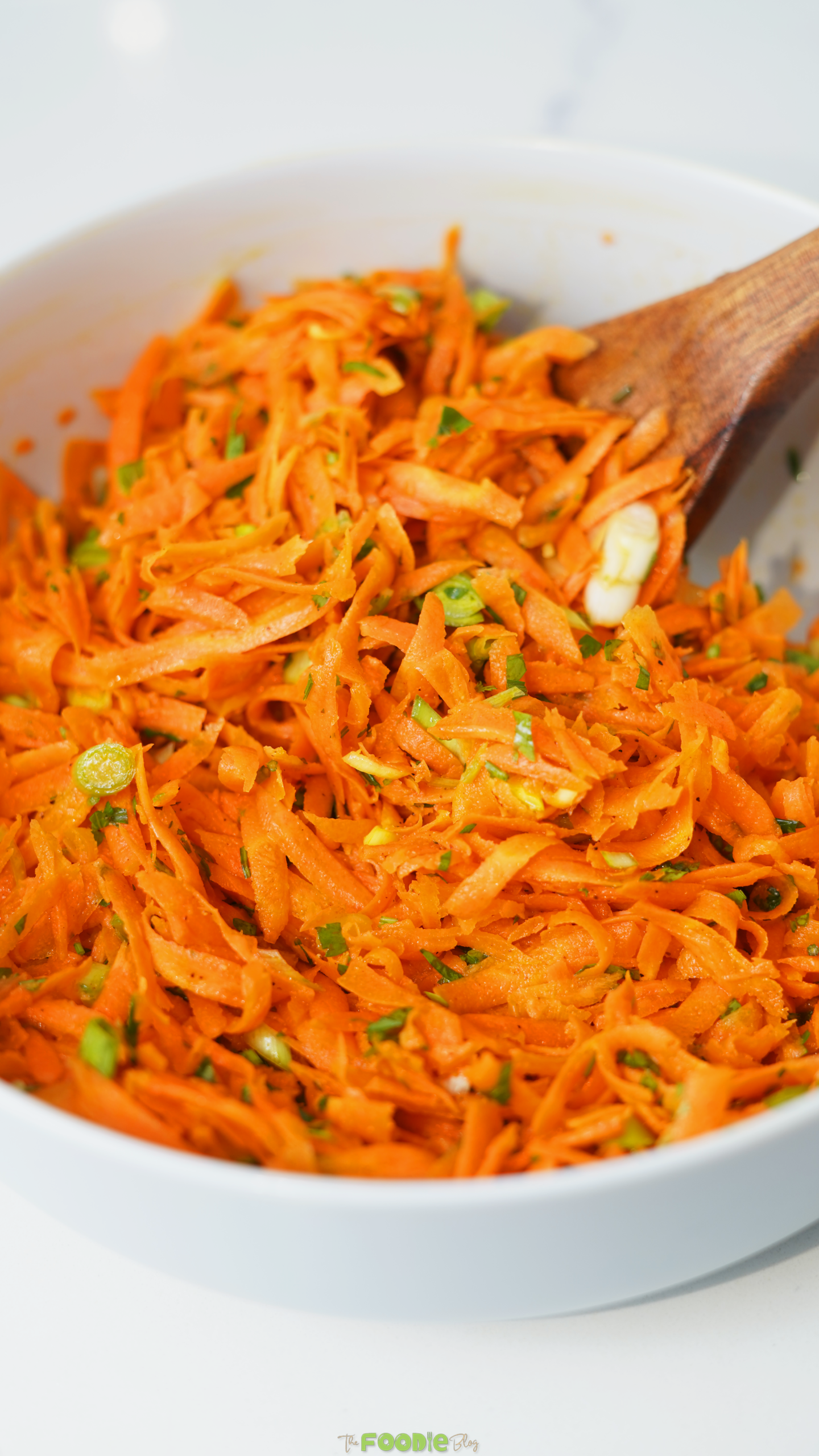 Close-up of shredded carrots mixed with green onion, parsley, and honey Dijon dressing.