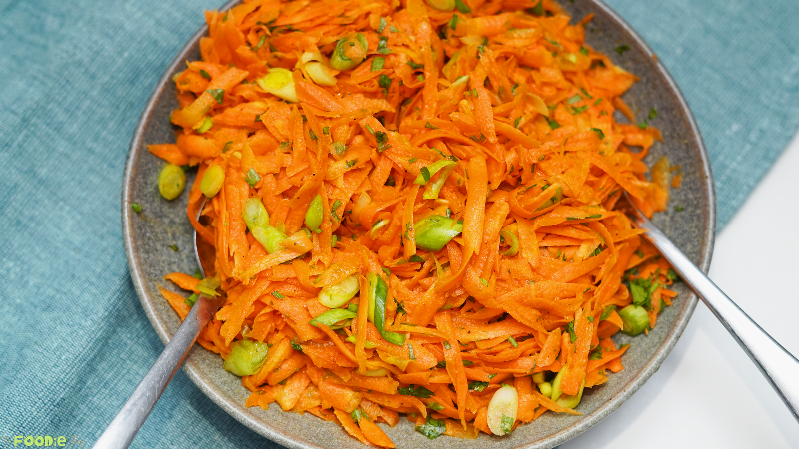 French carrot salad served on a gray plate with green onion and parsley on top.