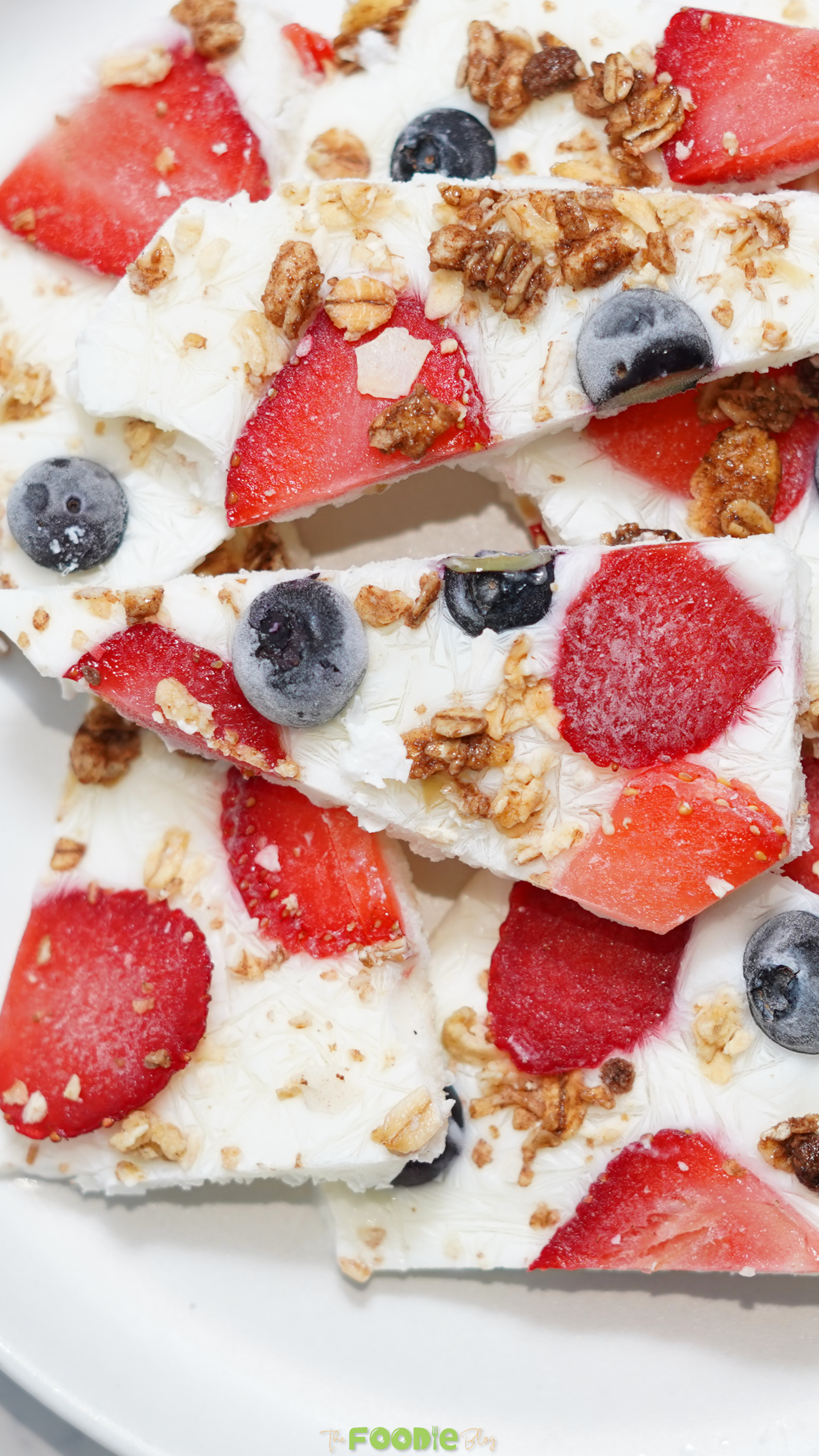 Close-up of frozen yogurt bark pieces with sliced strawberries, blueberries, and granola.