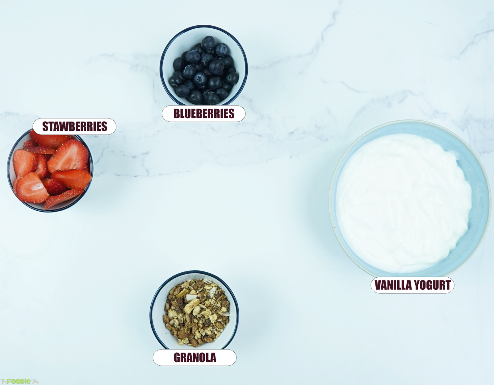 Ingredients for frozen yogurt bark including vanilla yogurt, strawberries, blueberries, and granola.