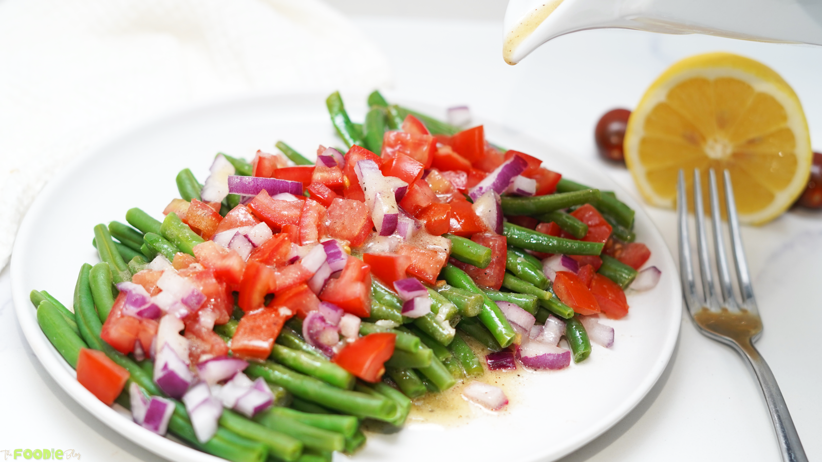 Lemon Dijon dressing being poured over green bean salad with tomato and red onion.