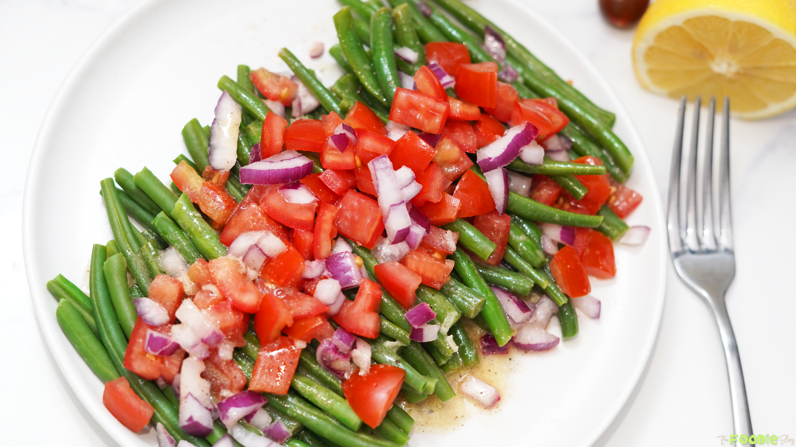 Green bean salad served on a white plate with diced tomato, red onion, and lemon dressing