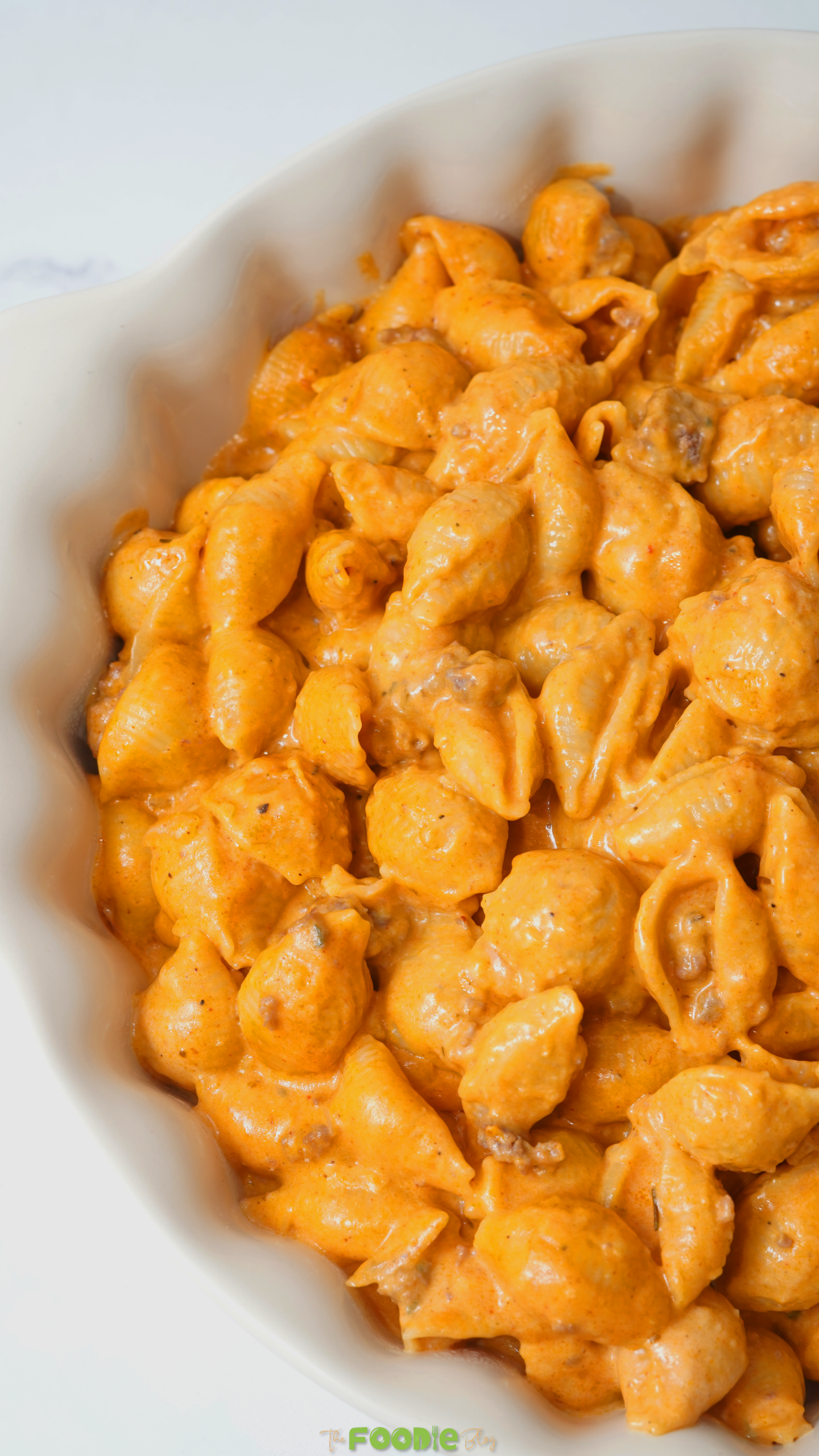 Close-up of pasta shells coated in creamy orange cheddar tomato sauce with small pieces of ground beef.