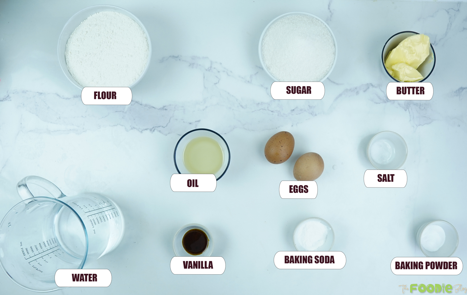 Ingredients for homemade vanilla cake including flour, sugar, butter, eggs, vanilla, water, oil, salt, baking soda, and baking powder.