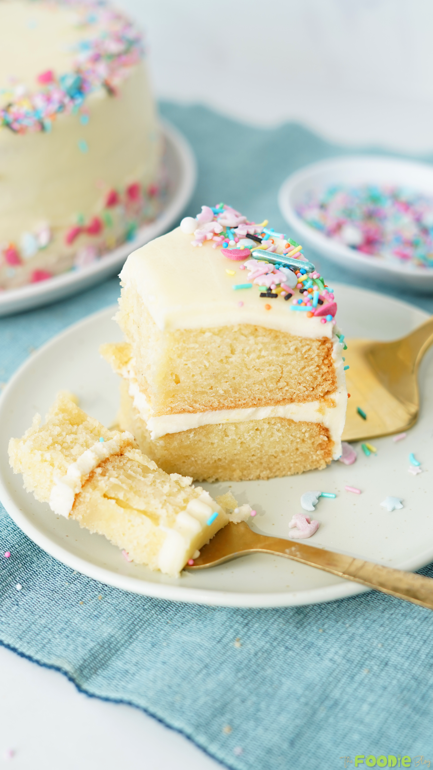 Slice of vanilla layer cake with buttercream frosting and rainbow sprinkles served on a white plate.