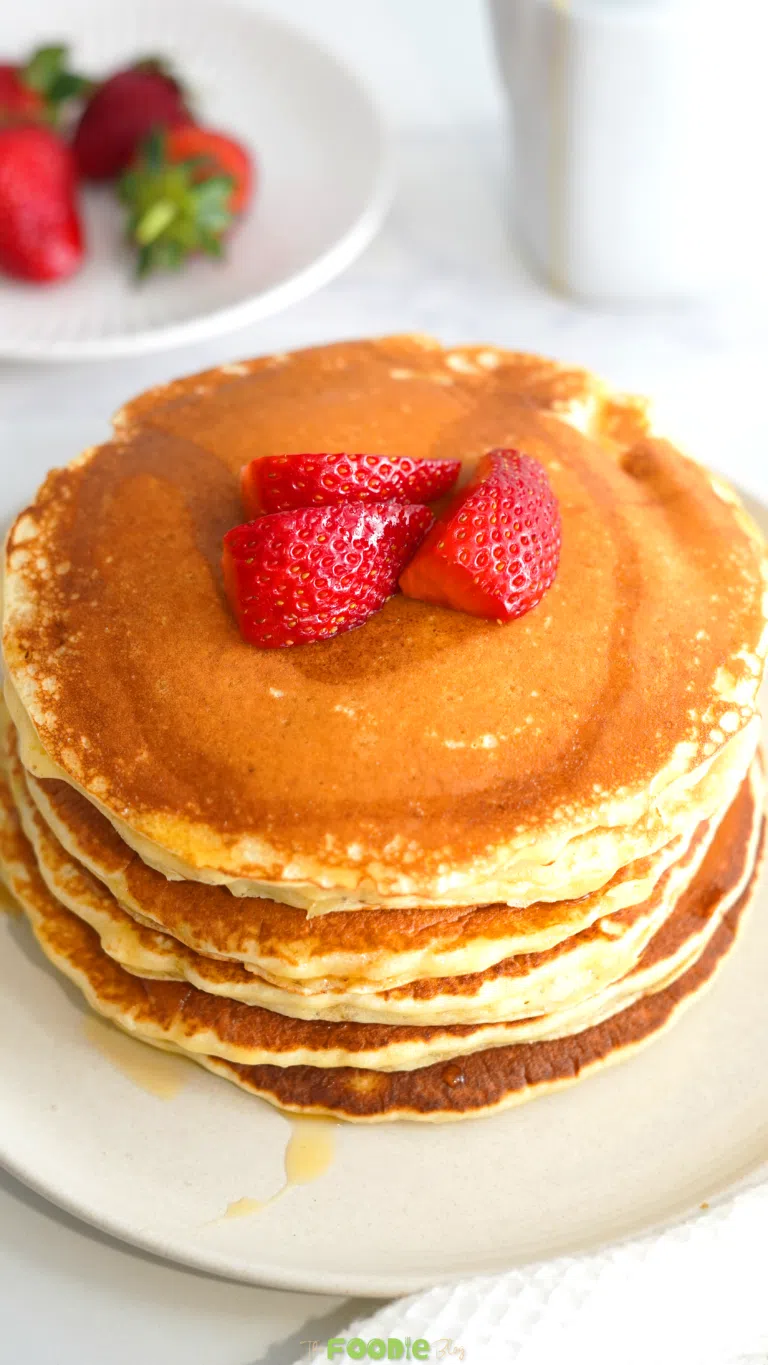 Close-up of fluffy golden protein pancakes topped with sliced strawberries and syrup.
