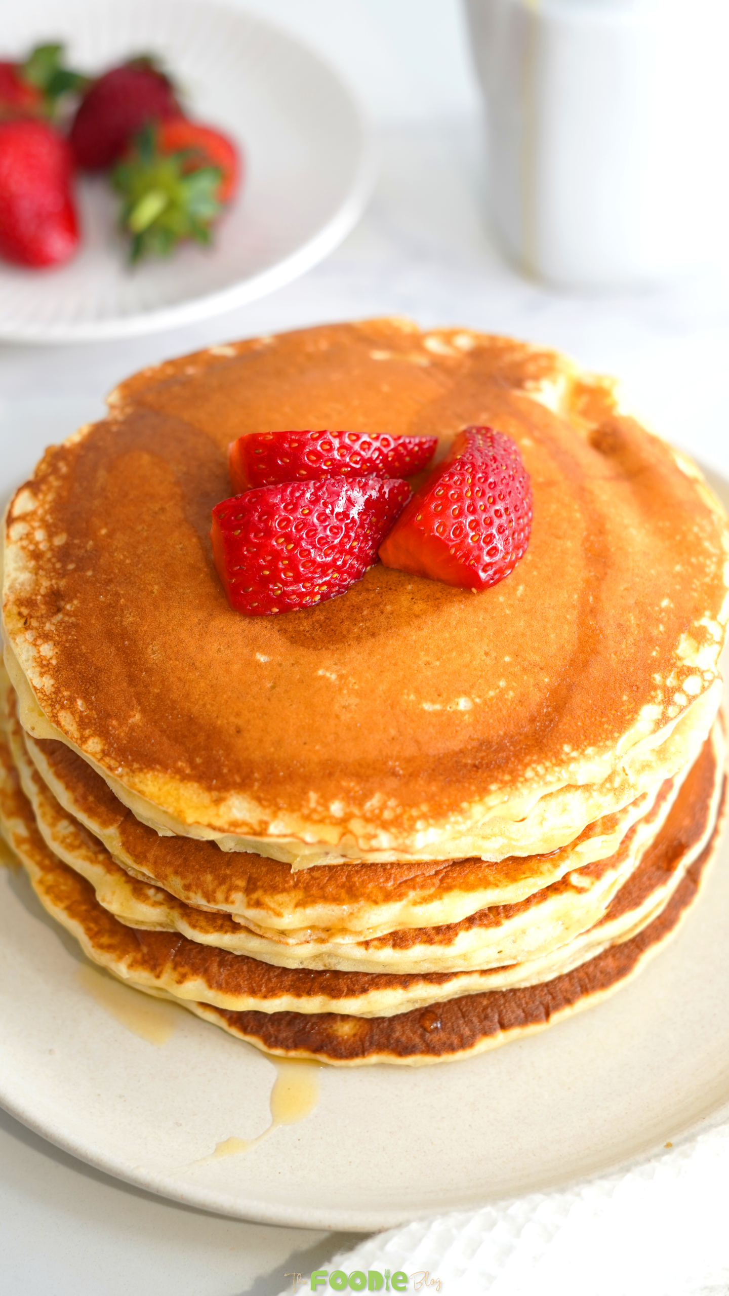 Close-up of fluffy golden protein pancakes topped with sliced strawberries and syrup.