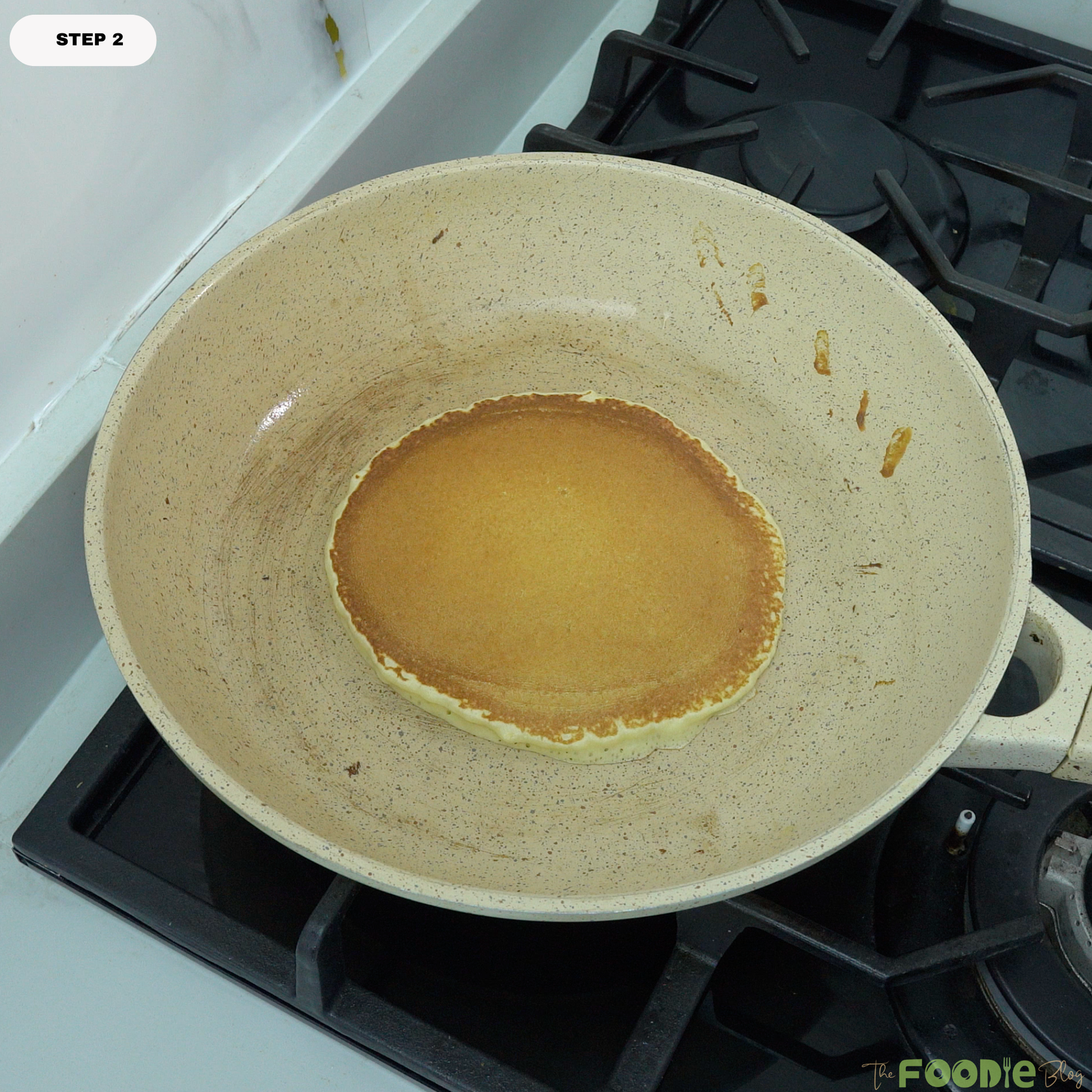 A golden protein pancake cooking in a nonstick skillet on the stovetop