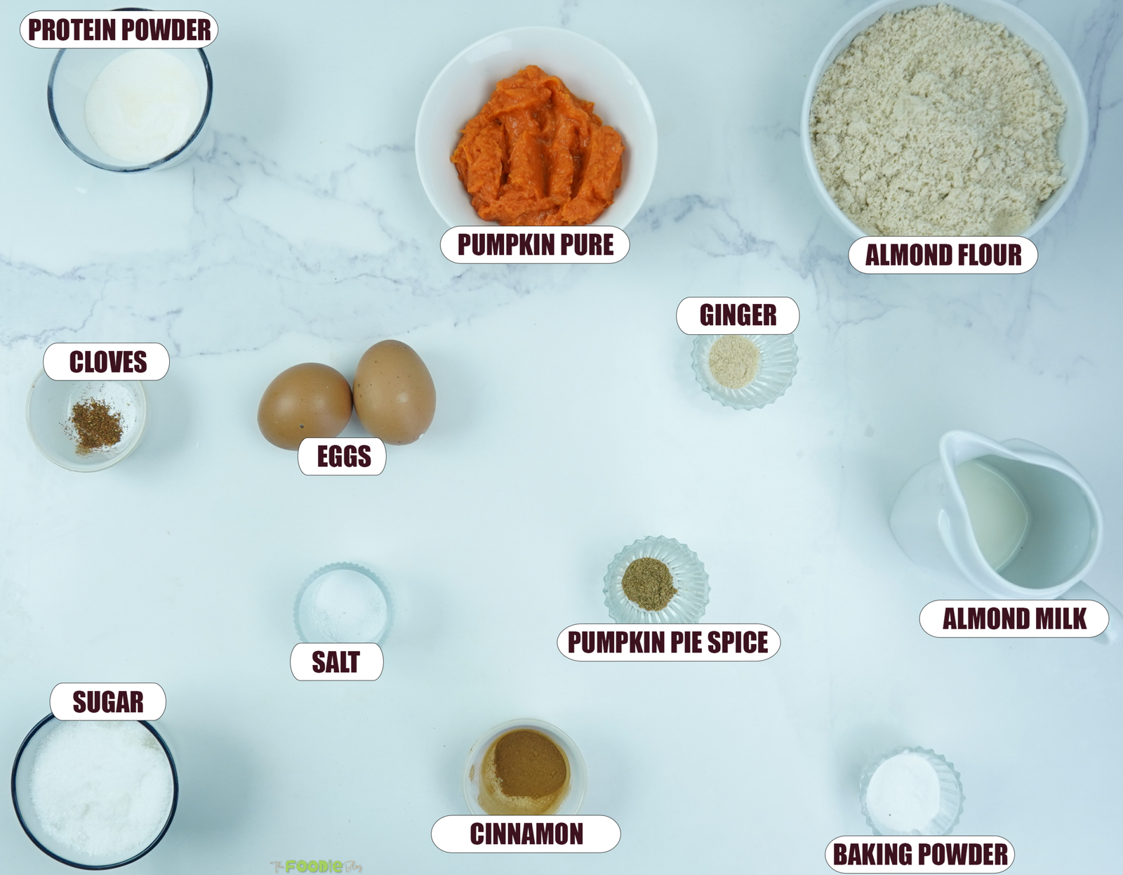 Ingredients for pumpkin protein muffins including pumpkin puree, almond flour, eggs, protein powder, almond milk, spices, sugar, salt, and baking powder.