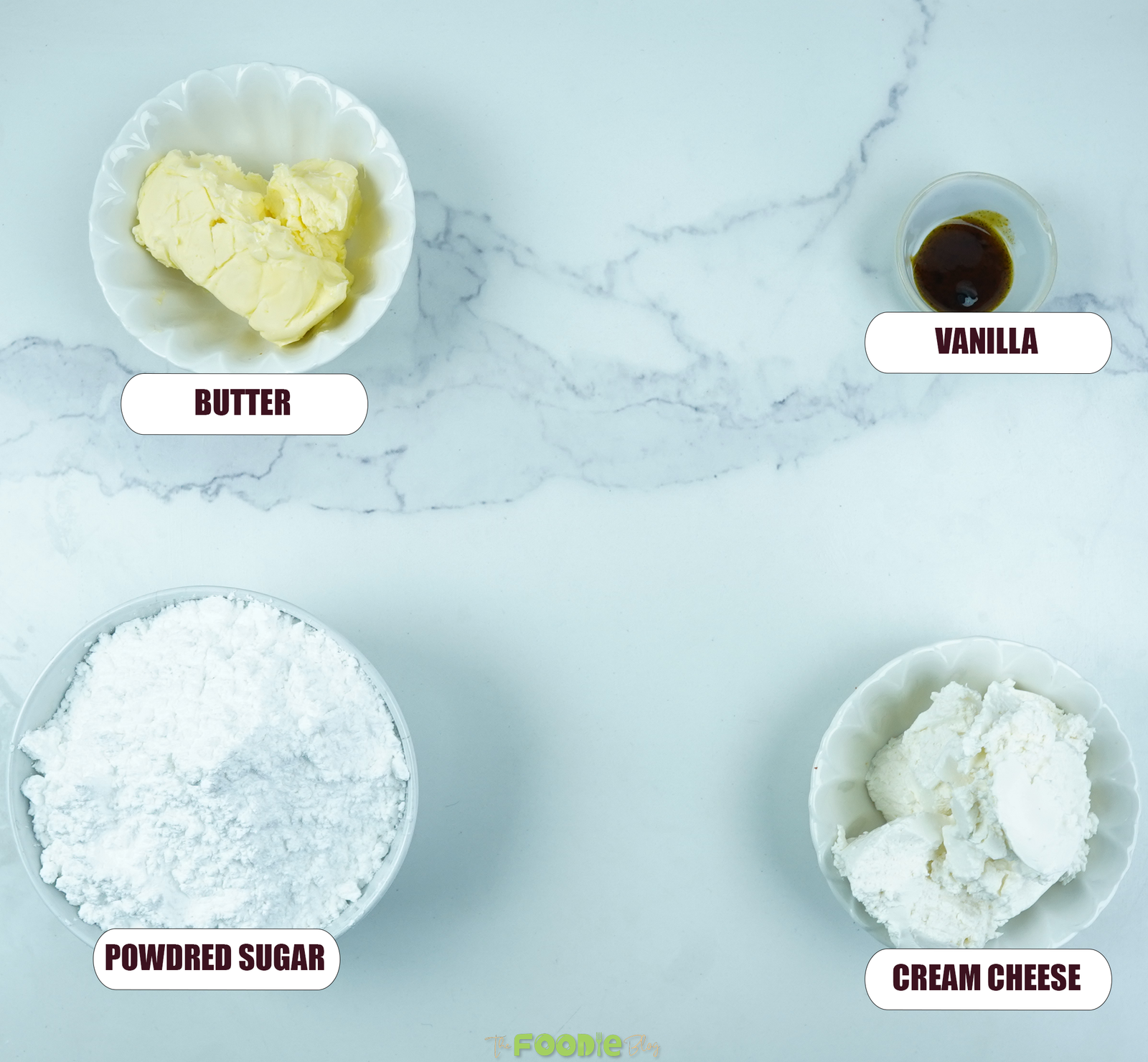 Butter, cream cheese, powdered sugar, and vanilla arranged on a white marble surface for red velvet cake frosting.