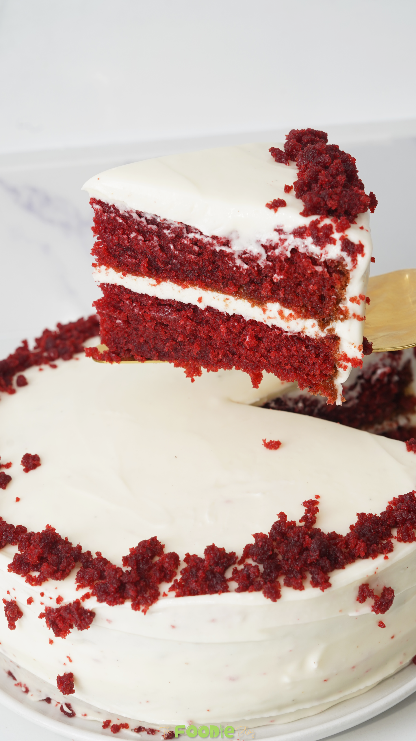 A slice of red velvet cake with cream cheese frosting being lifted from a frosted layer cake.