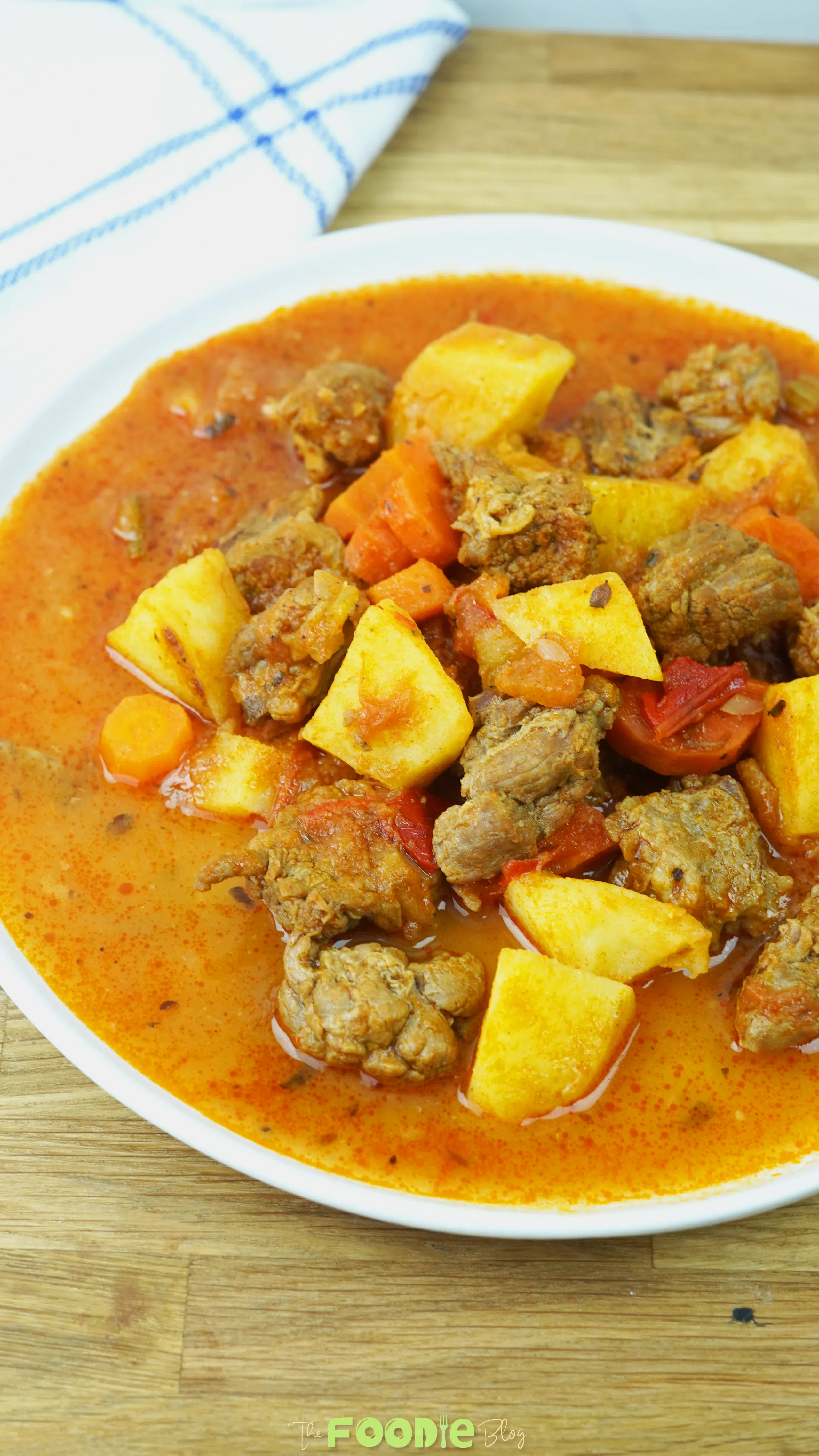 Close-up of beef stew with tender beef, potatoes, carrots, tomatoes, and a rich paprika-colored broth.