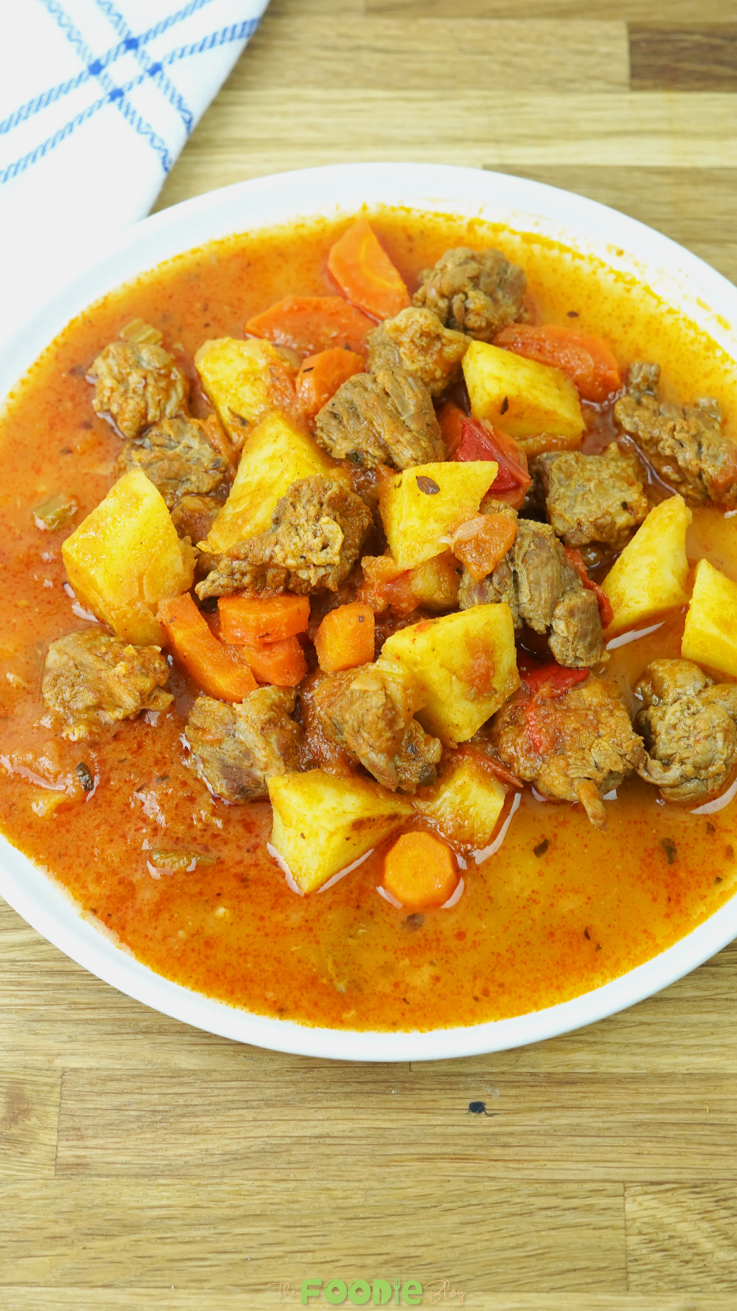 Bowl of beef stew with tender beef chunks, potatoes, carrots, and tomato broth served on a wooden board.