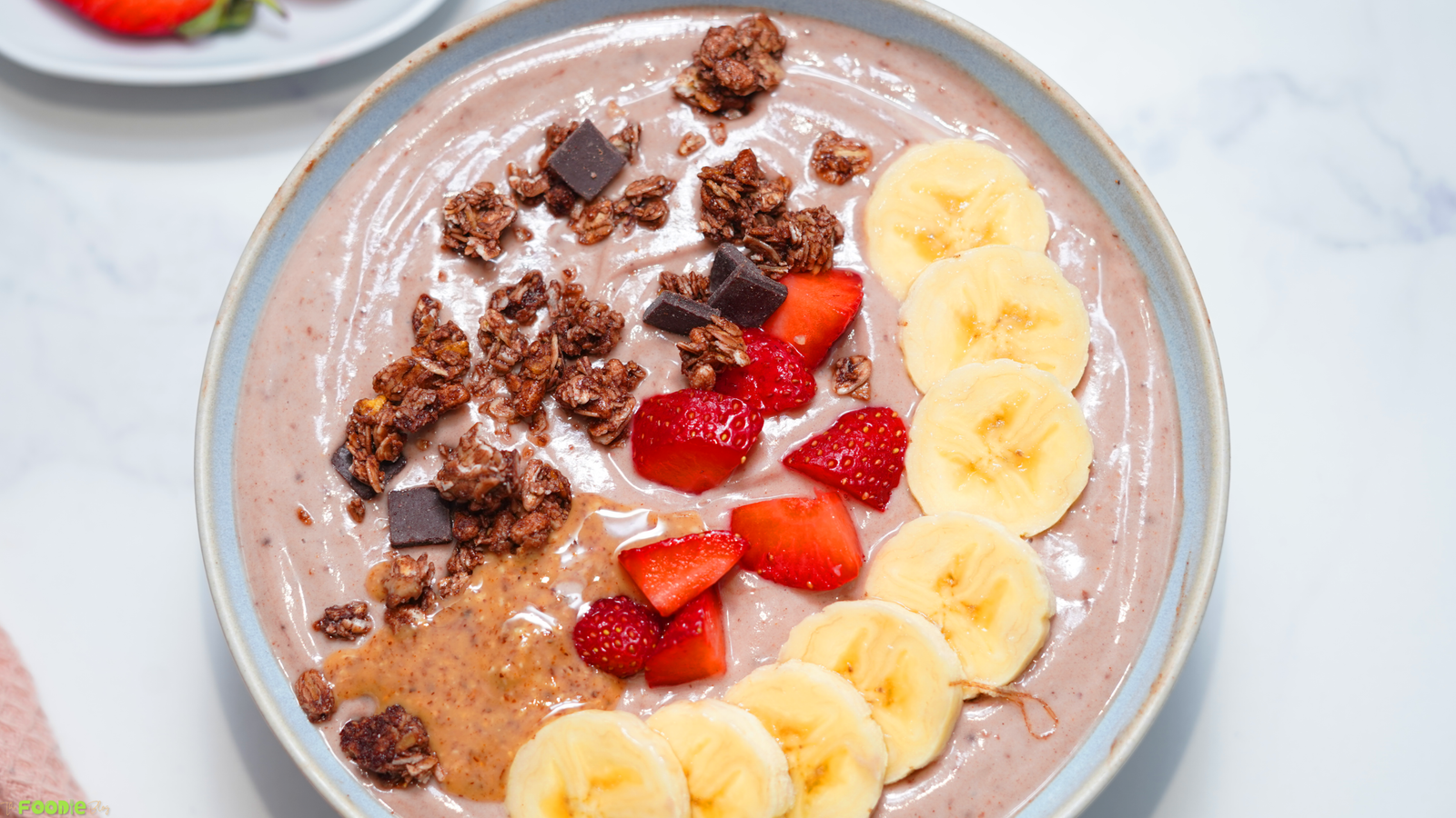 High-protein Greek yogurt bowl topped with banana slices, strawberries, granola, peanut butter, and chocolate chunks