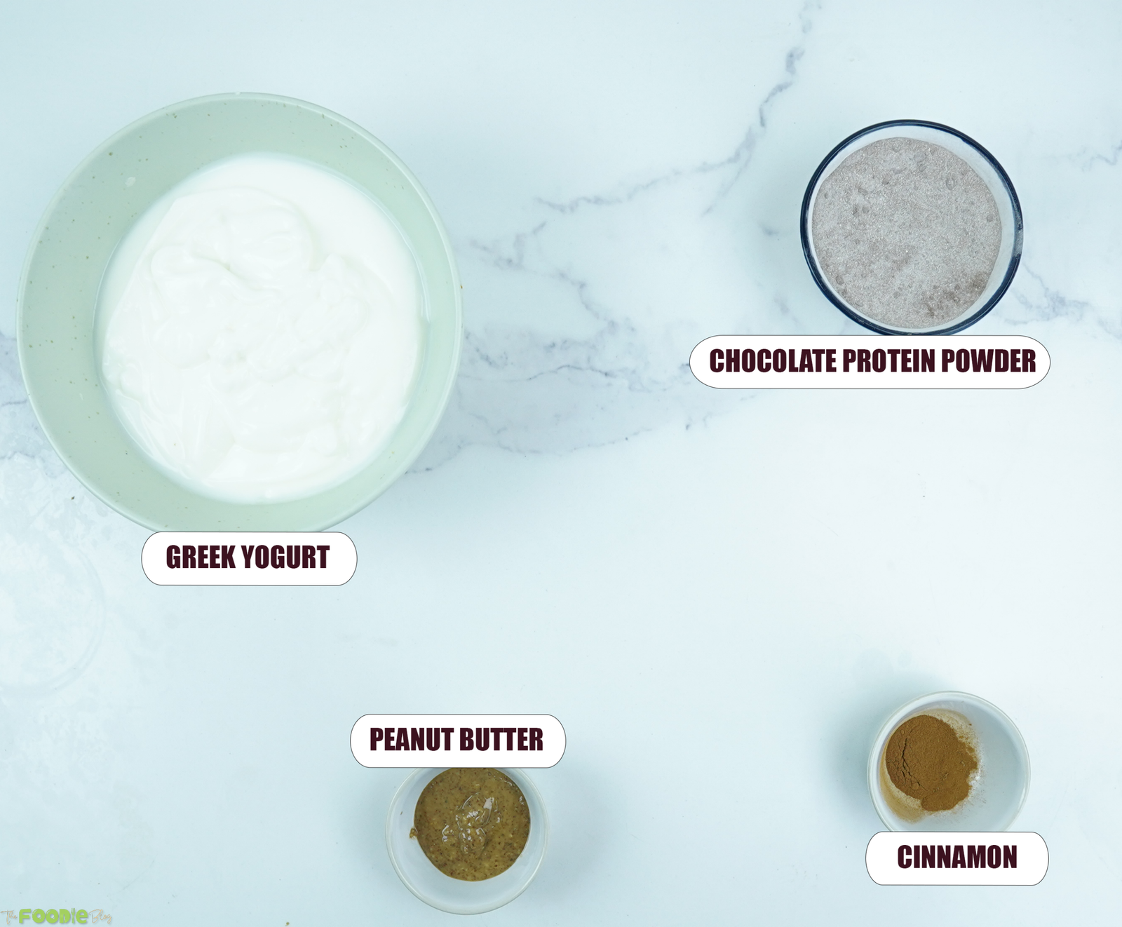 Greek yogurt bowl ingredients: plain Greek yogurt, chocolate protein powder, peanut butter, cinnamon, banana, strawberries, granola, and chocolate chunks