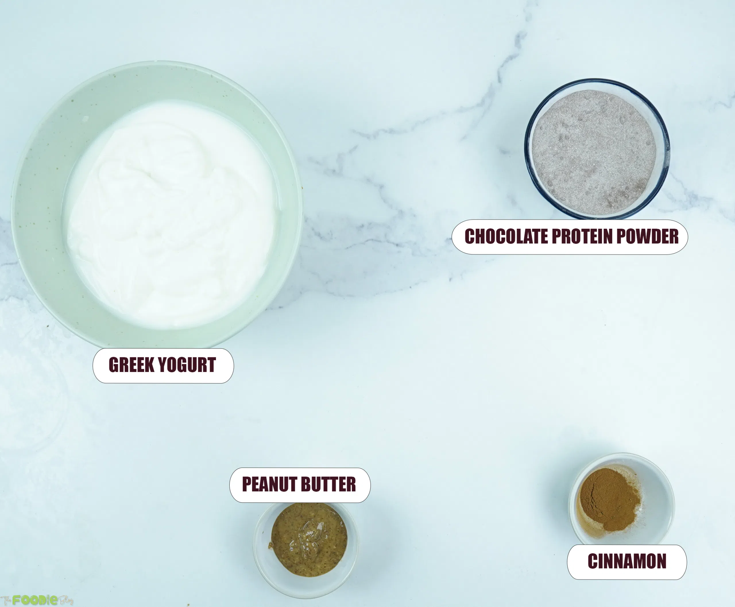 Greek yogurt bowl ingredients: plain Greek yogurt, chocolate protein powder, peanut butter, cinnamon, banana, strawberries, granola, and chocolate chunks