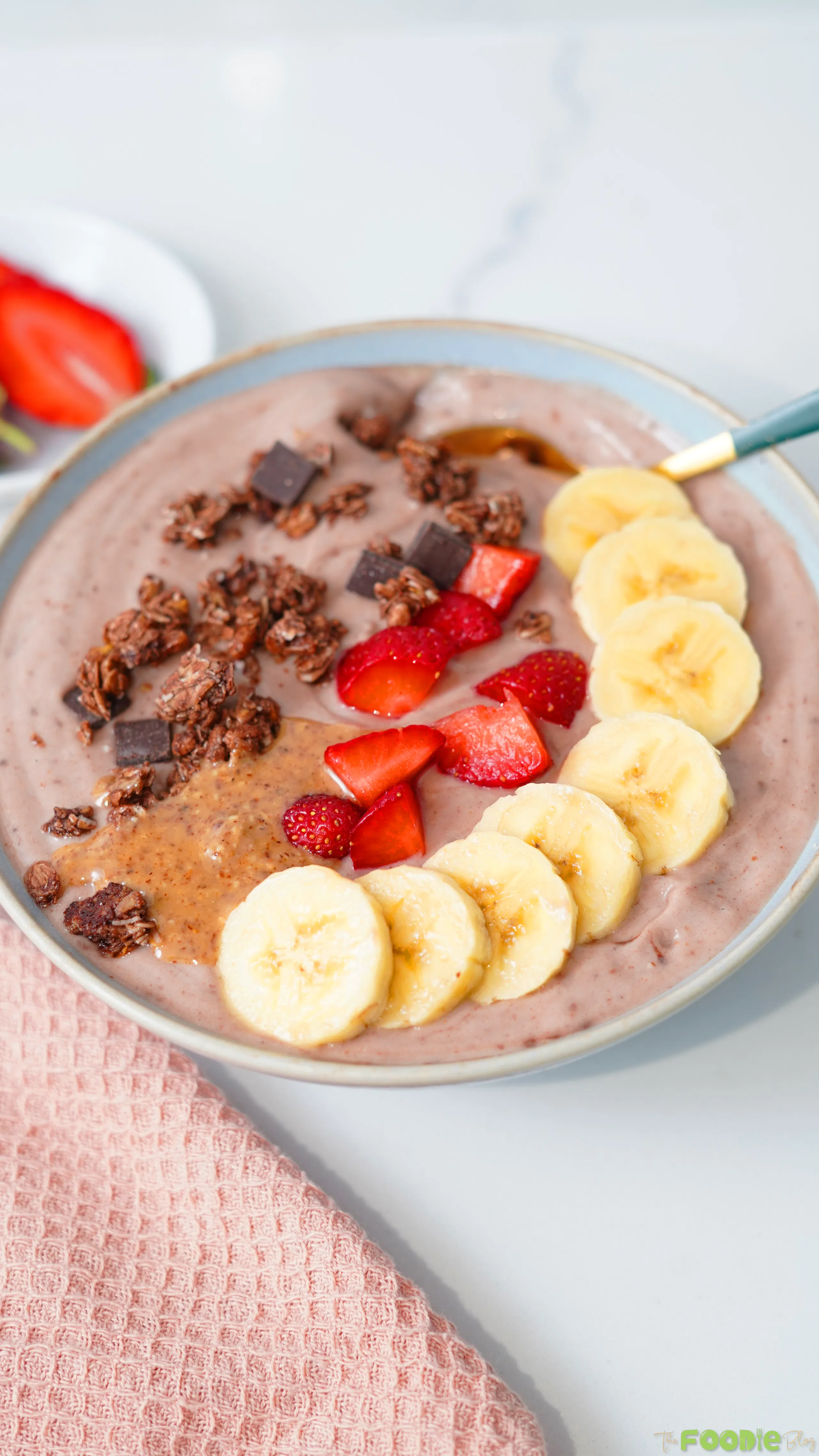 Protein-packed yogurt bowl served with banana slices, strawberries, granola, peanut butter, and a spoon.