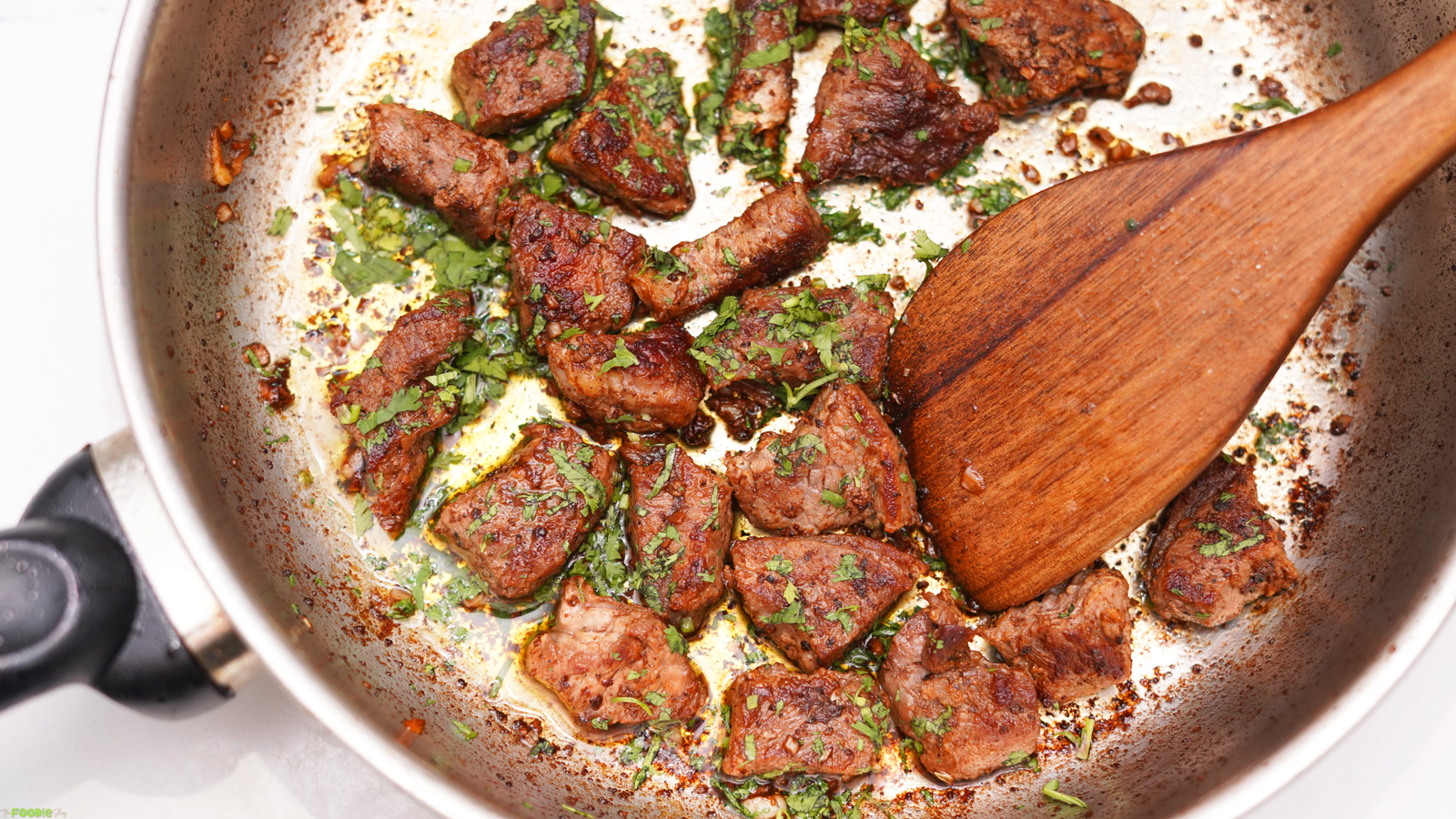 Steak bites seared in a skillet with garlic butter and fresh parsley.
