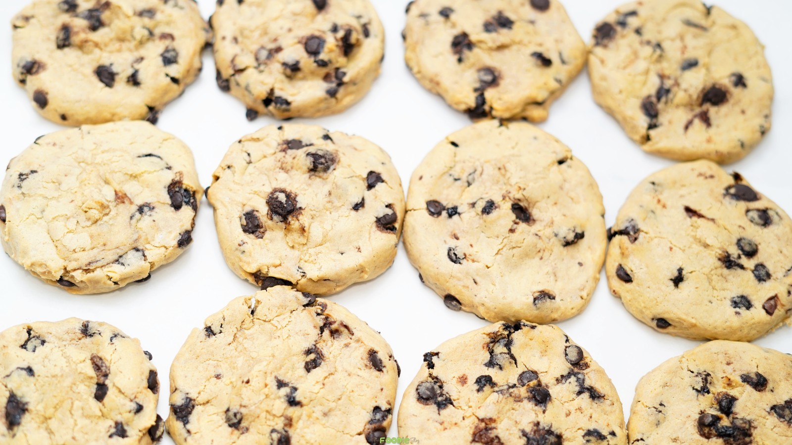 Freshly baked chocolate chip cookies arranged on a white surface with chocolate chips throughout.