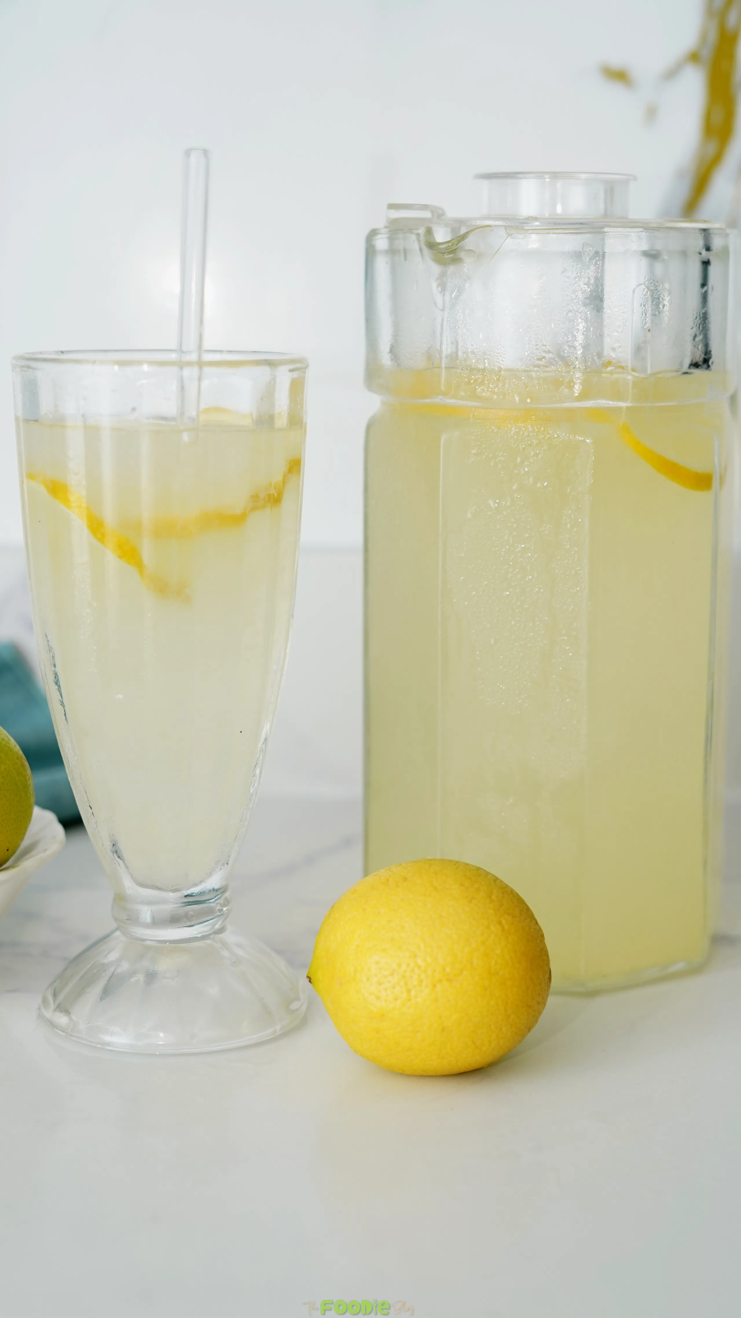Fresh homemade lemonade served in a tall glass beside a pitcher with lemon slices.