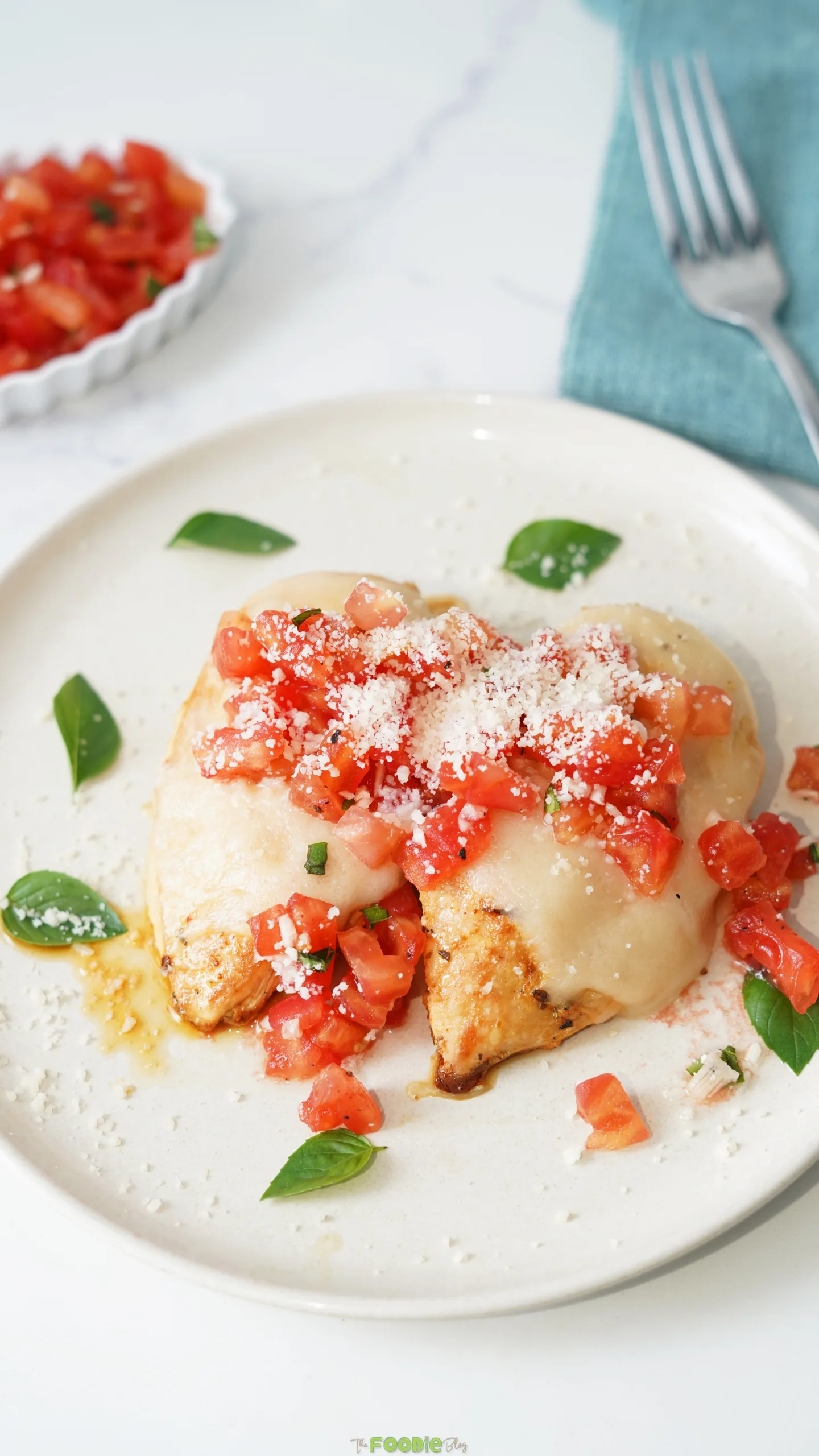 Close-up of Bruschetta Chicken with melted mozzarella, diced tomatoes, Parmesan, basil, and pan juices.