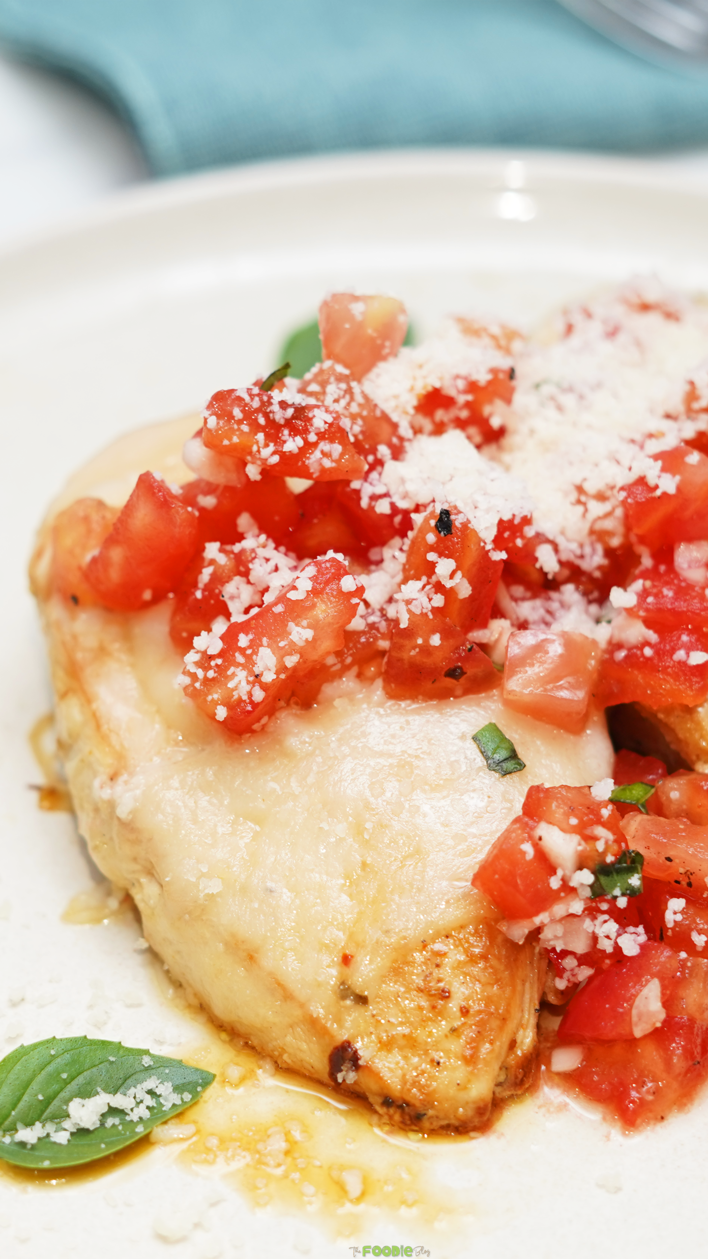 Close-up of Bruschetta Chicken with melted mozzarella, chopped tomatoes, Parmesan, garlic, and basil.