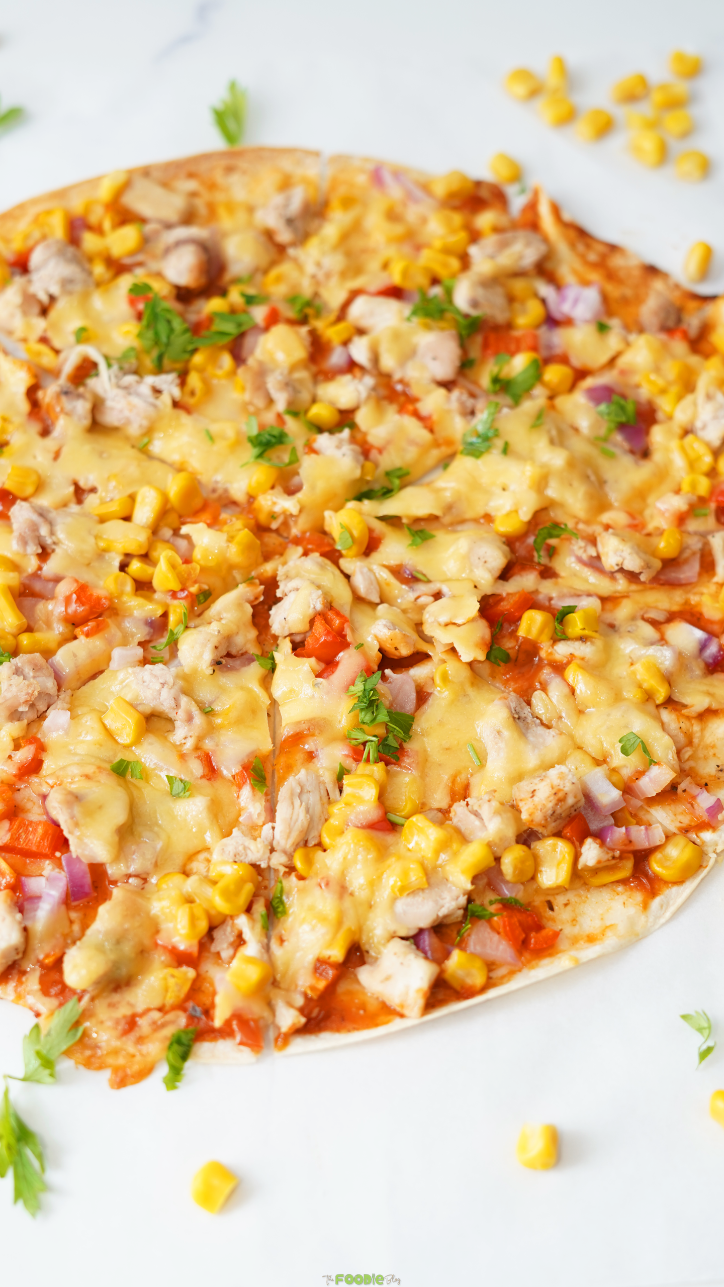 Close-up of a cheesy Mexican flatbread pizza with chicken, corn, red onion, and bell pepper.