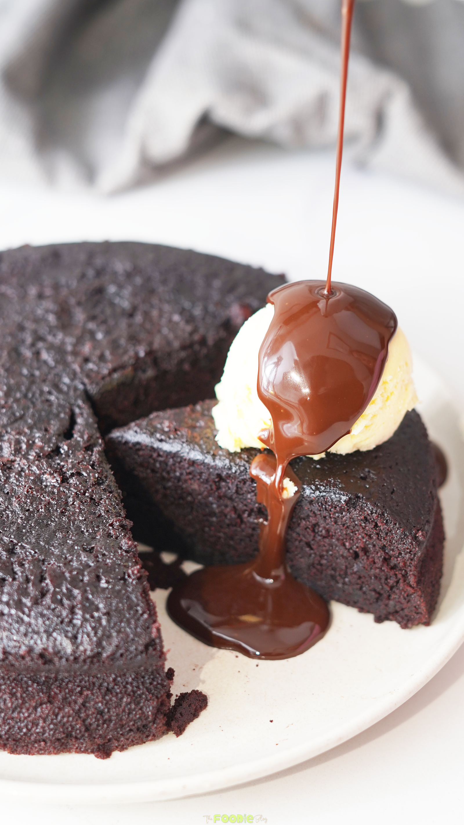 Chocolate sauce pouring over vanilla ice cream on a warm chocolate cake slice.