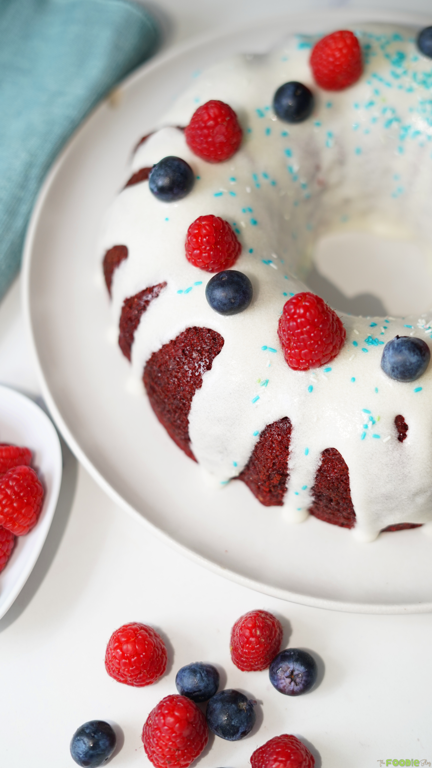 Close-up of cream cheese glaze dripping over red velvet Bundt cake with berries.