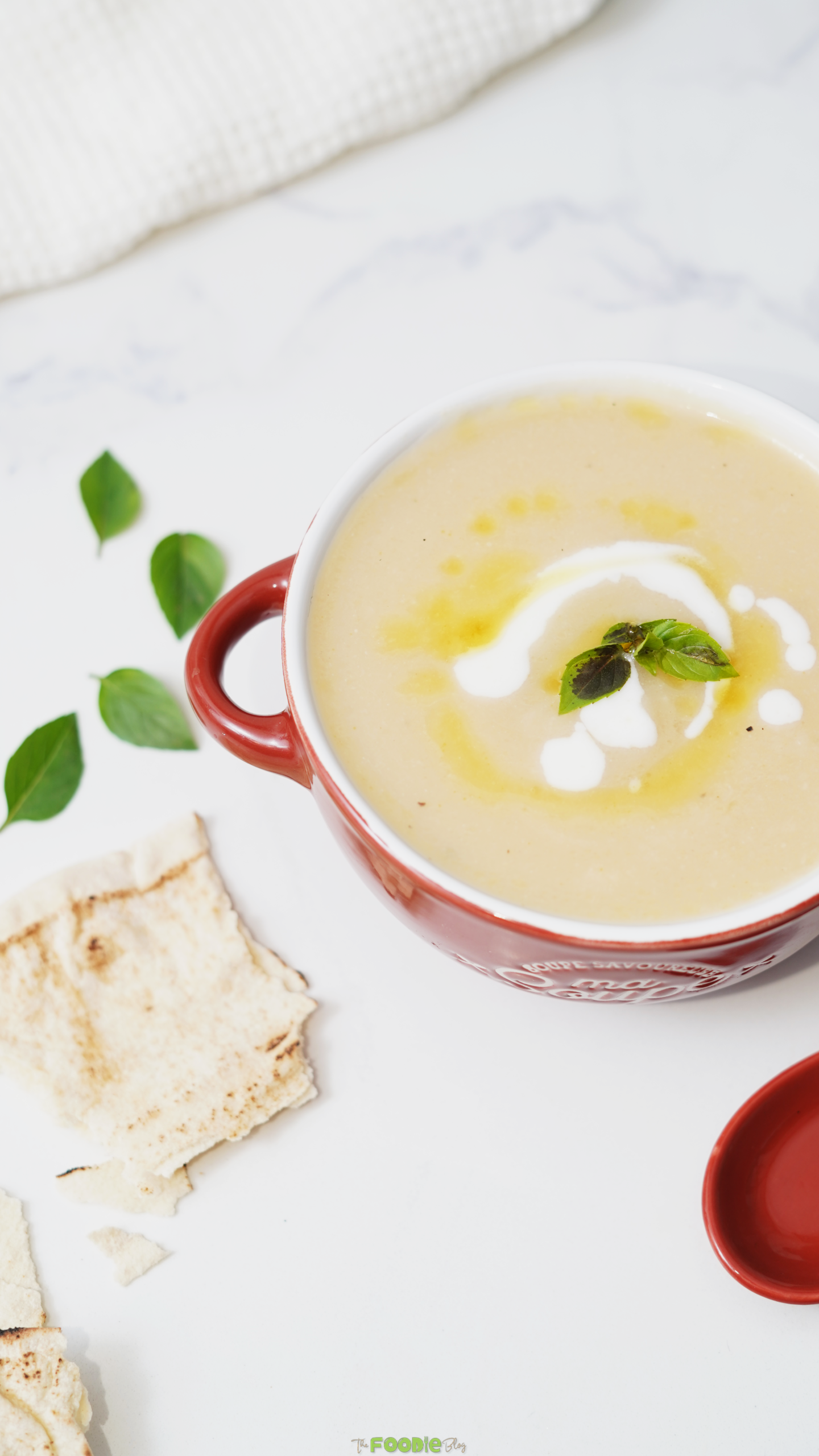 Creamy cauliflower soup in a red bowl served with toasted pita and fresh basil leaves.