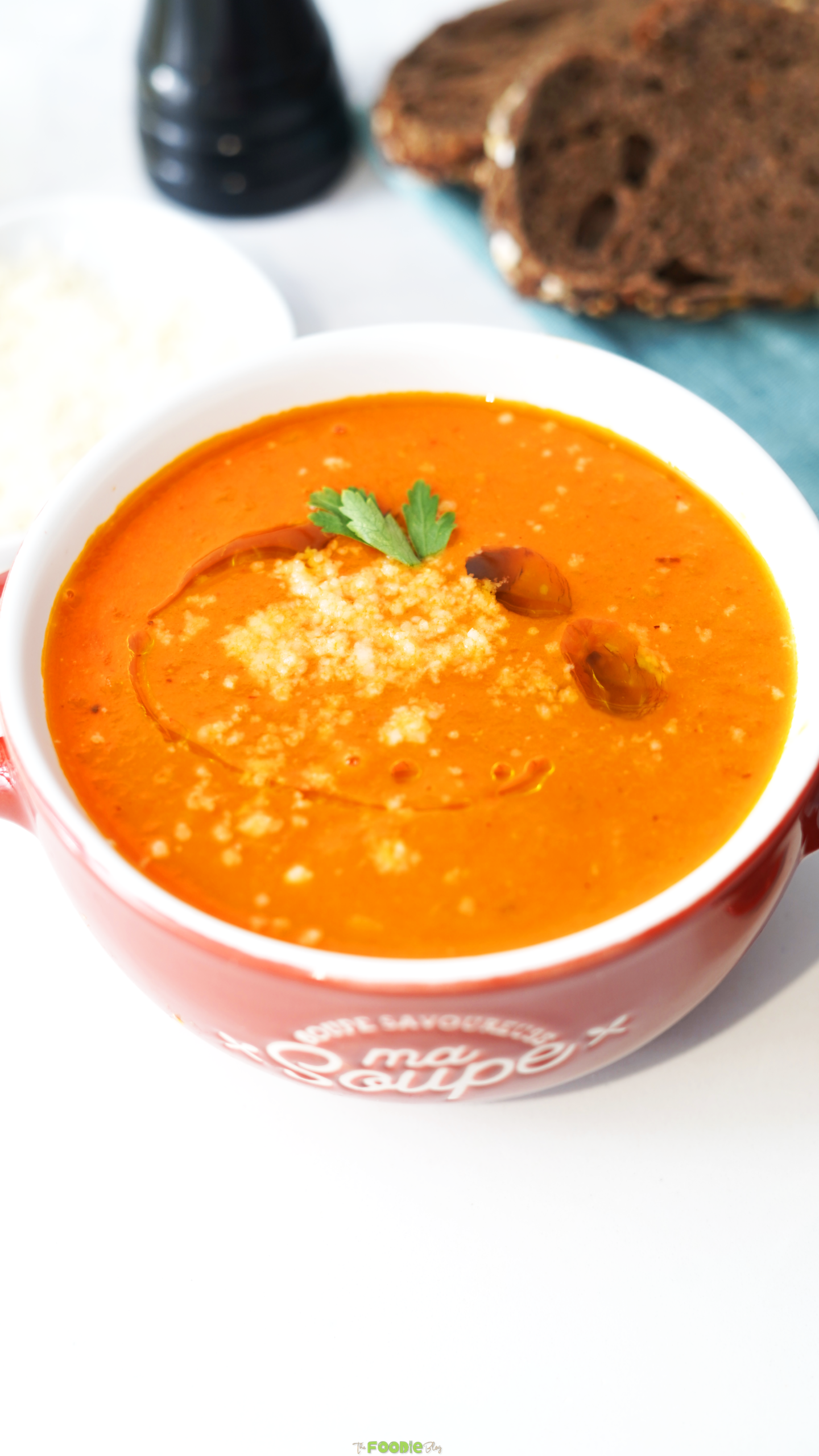 Bowl of creamy tomato soup topped with parmesan, olive oil, and a fresh herb leaf.