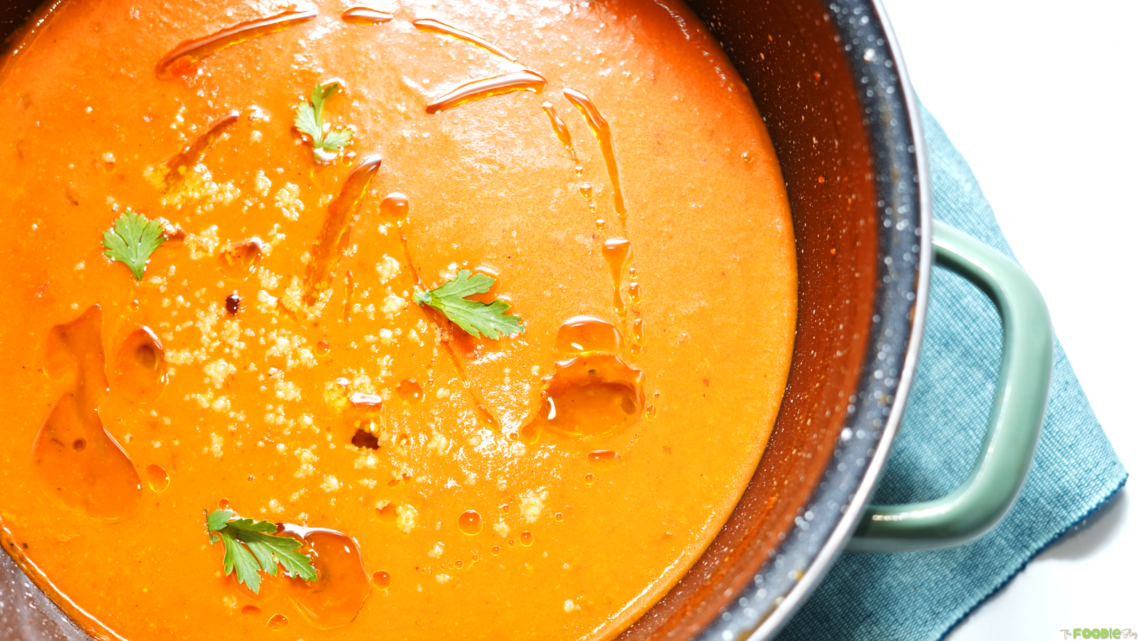 Pot of creamy tomato soup topped with olive oil, parmesan cheese, and fresh herb leaves