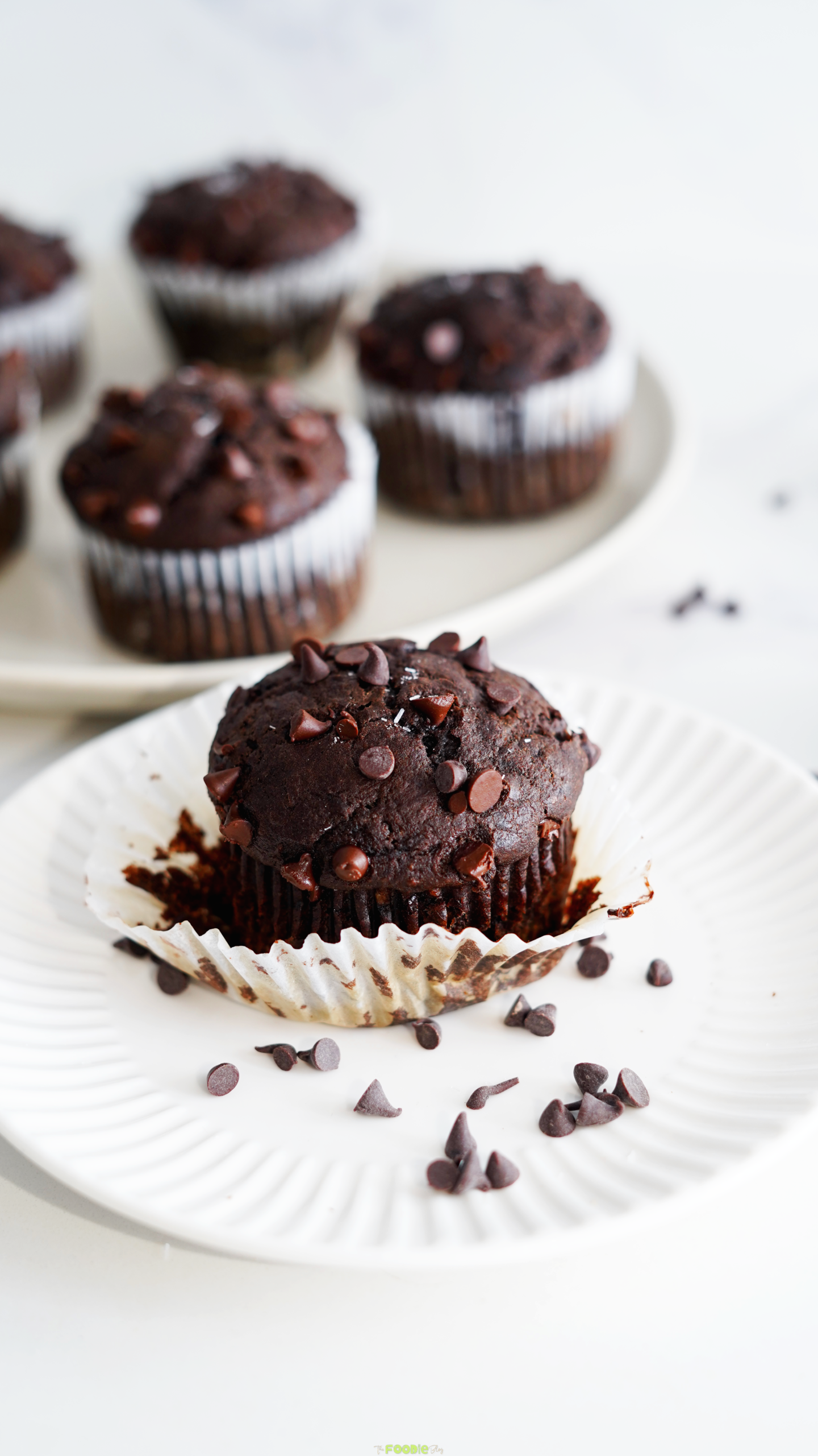 Close-up of one double chocolate protein muffin on a white plate with chocolate chips scattered around.
