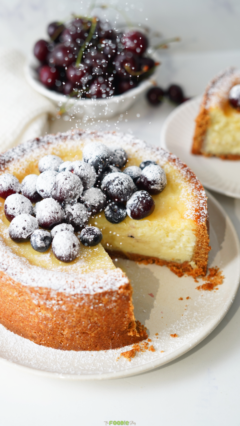 Easy Classic Baked Cheesecake topped with blueberries, cherries, and powdered sugar.