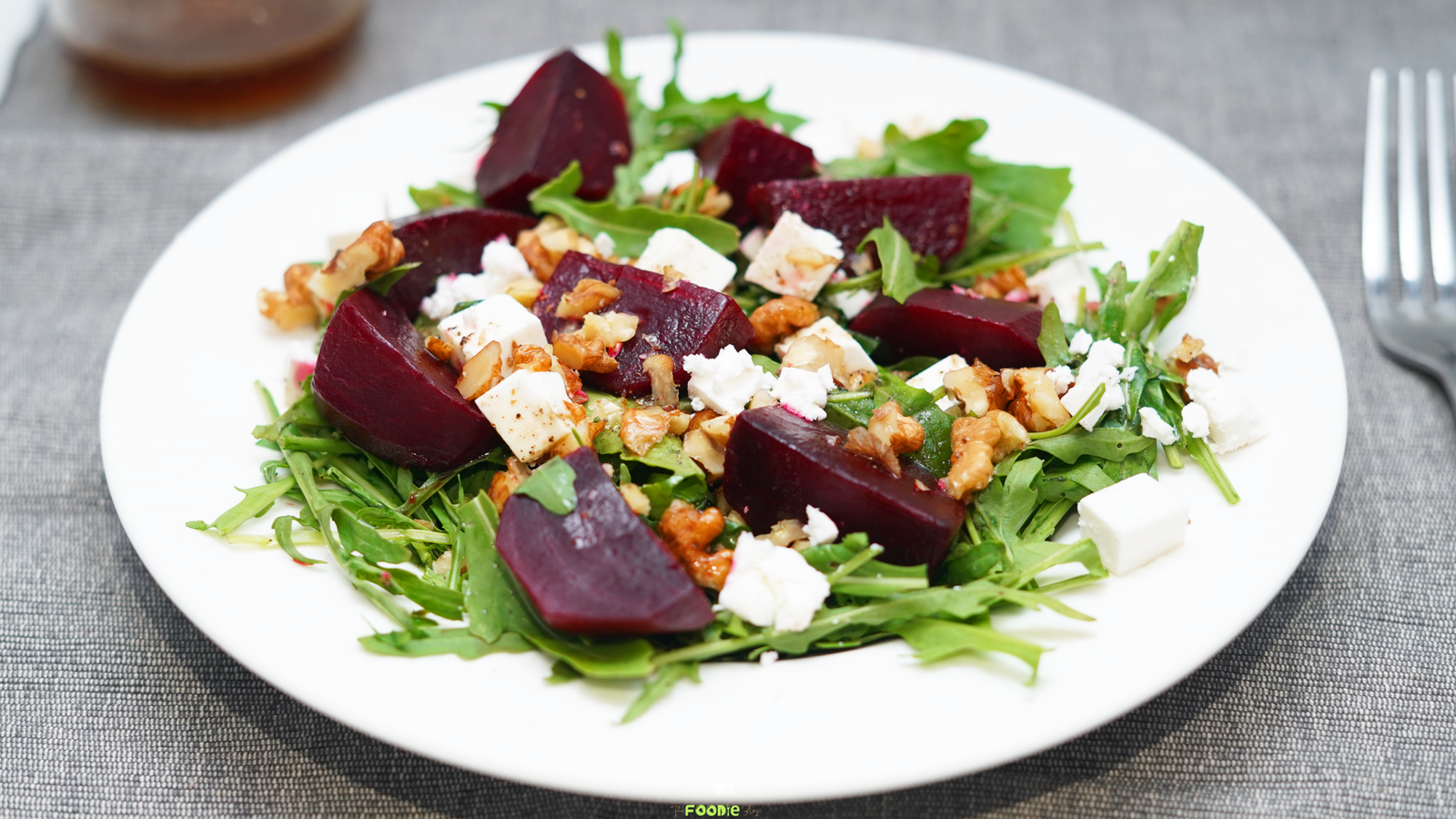 Beet salad with arugula, feta, walnuts, and honey balsamic dressing on a white plate.