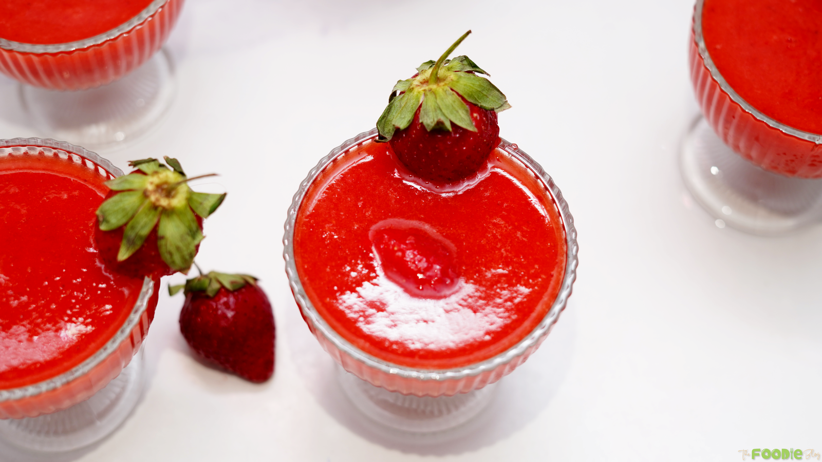 Several frozen strawberry daiquiri glasses arranged on a white surface with fresh strawberry garnish.