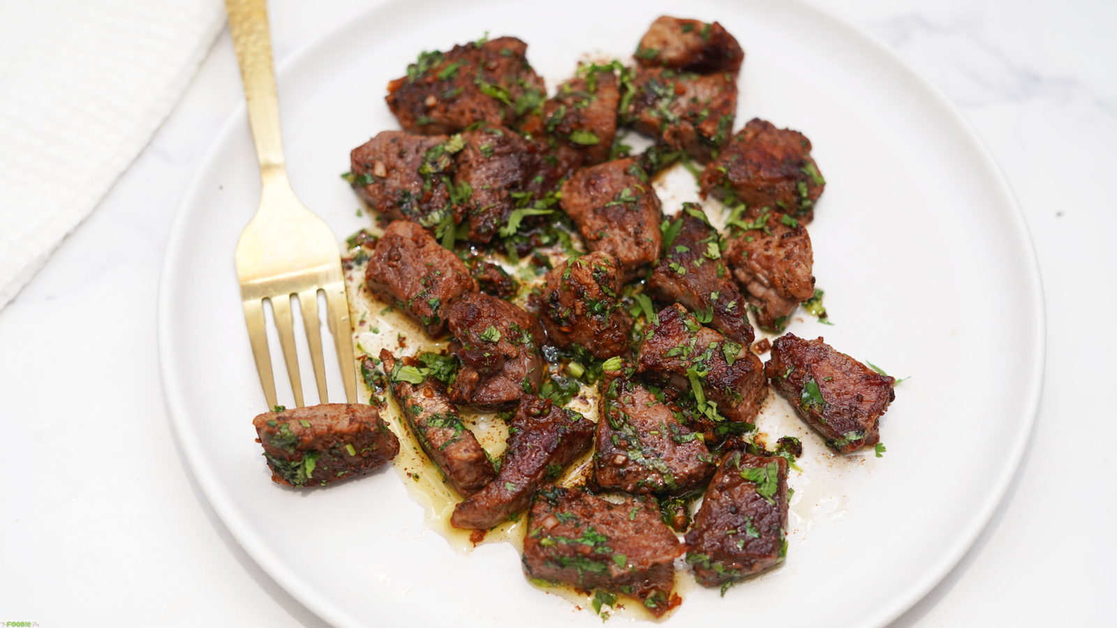 Plate of Garlic Butter Steak Bites with chopped parsley, garlic butter sauce, and a gold fork