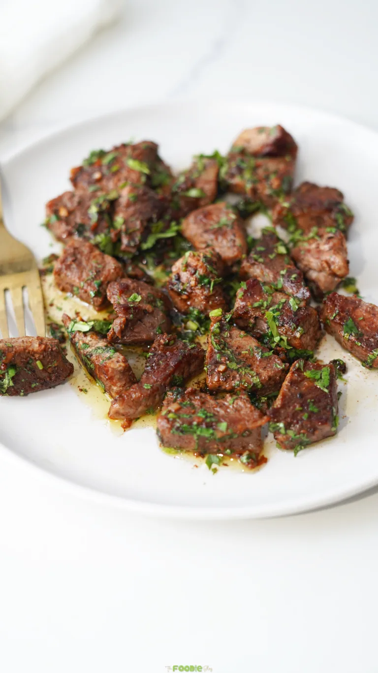 Garlic Butter Steak Bites served on a white plate with fresh parsley and melted butter sauce.