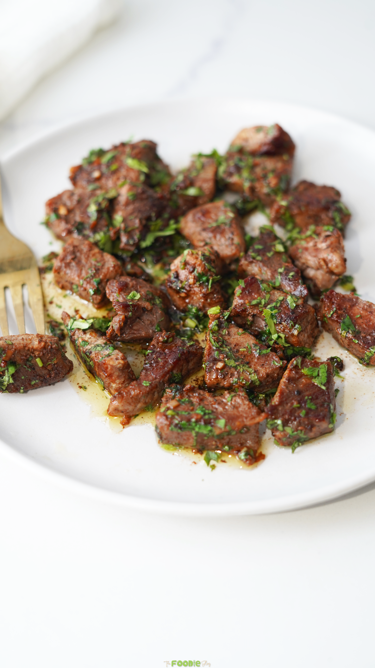 Garlic Butter Steak Bites served on a white plate with fresh parsley and melted butter sauce.