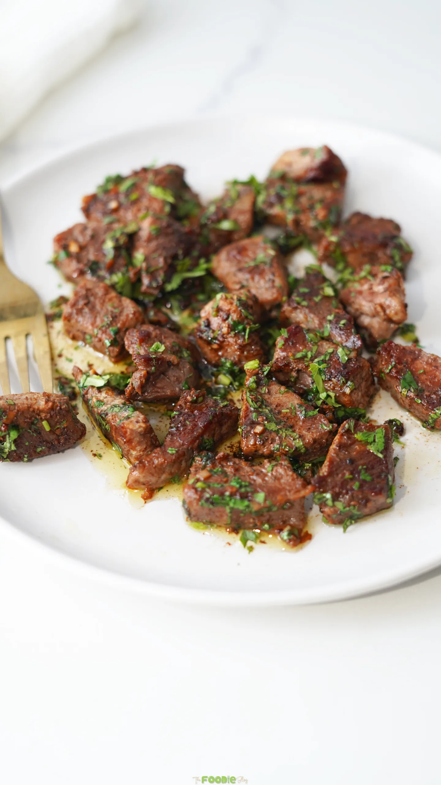 Garlic Butter Steak Bites served on a white plate with fresh parsley and melted butter sauce.