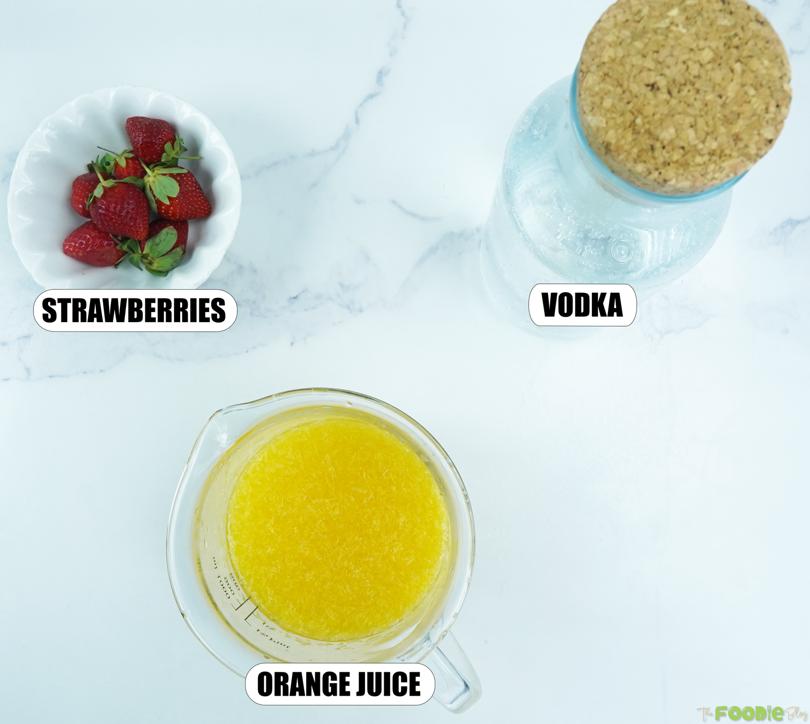 Ingredients for a vodka mimosa cocktail with strawberries, orange juice, and vodka on a white marble background.