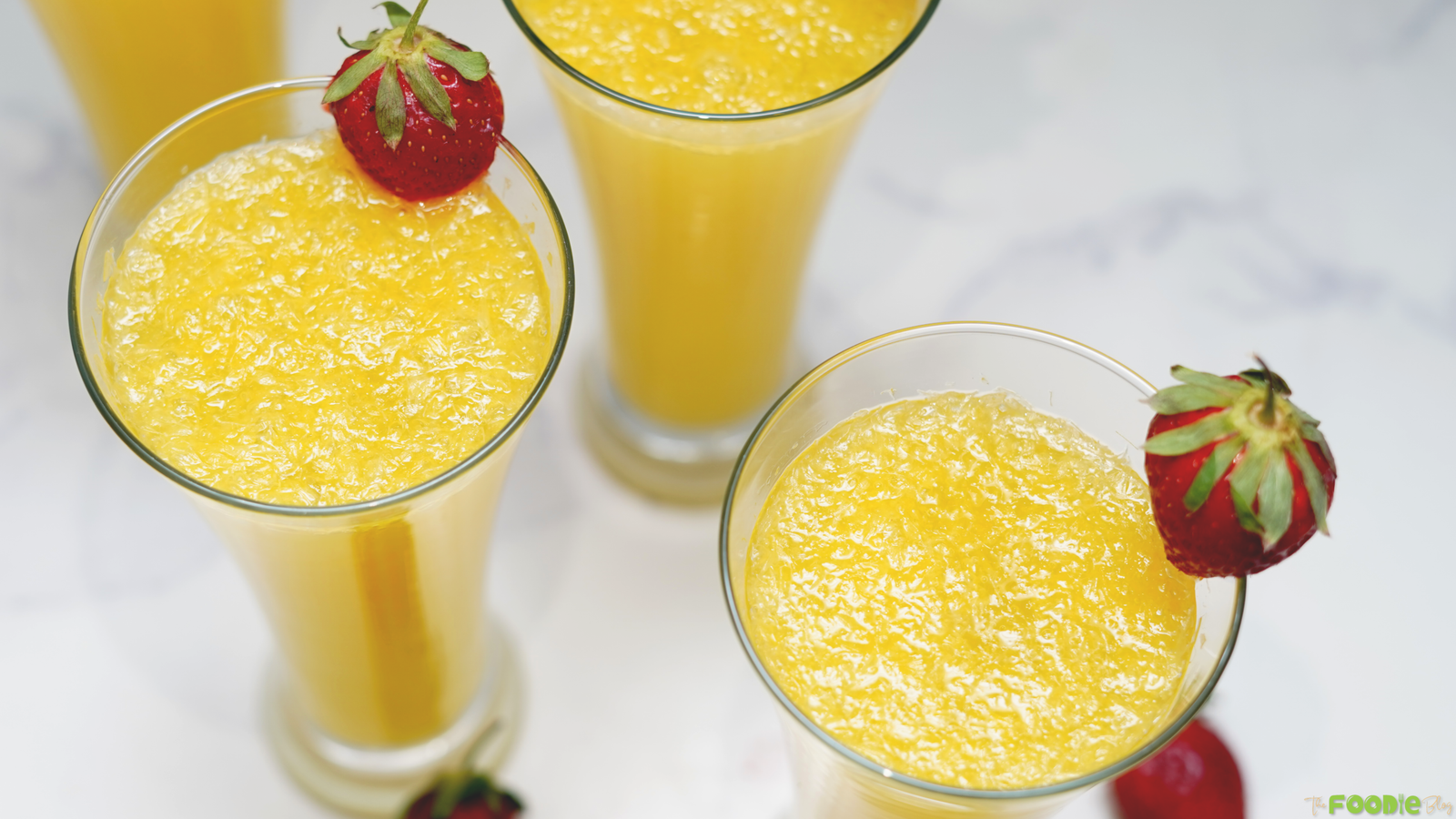 Overhead view of orange mimosa cocktails in glasses with fresh strawberry garnish.