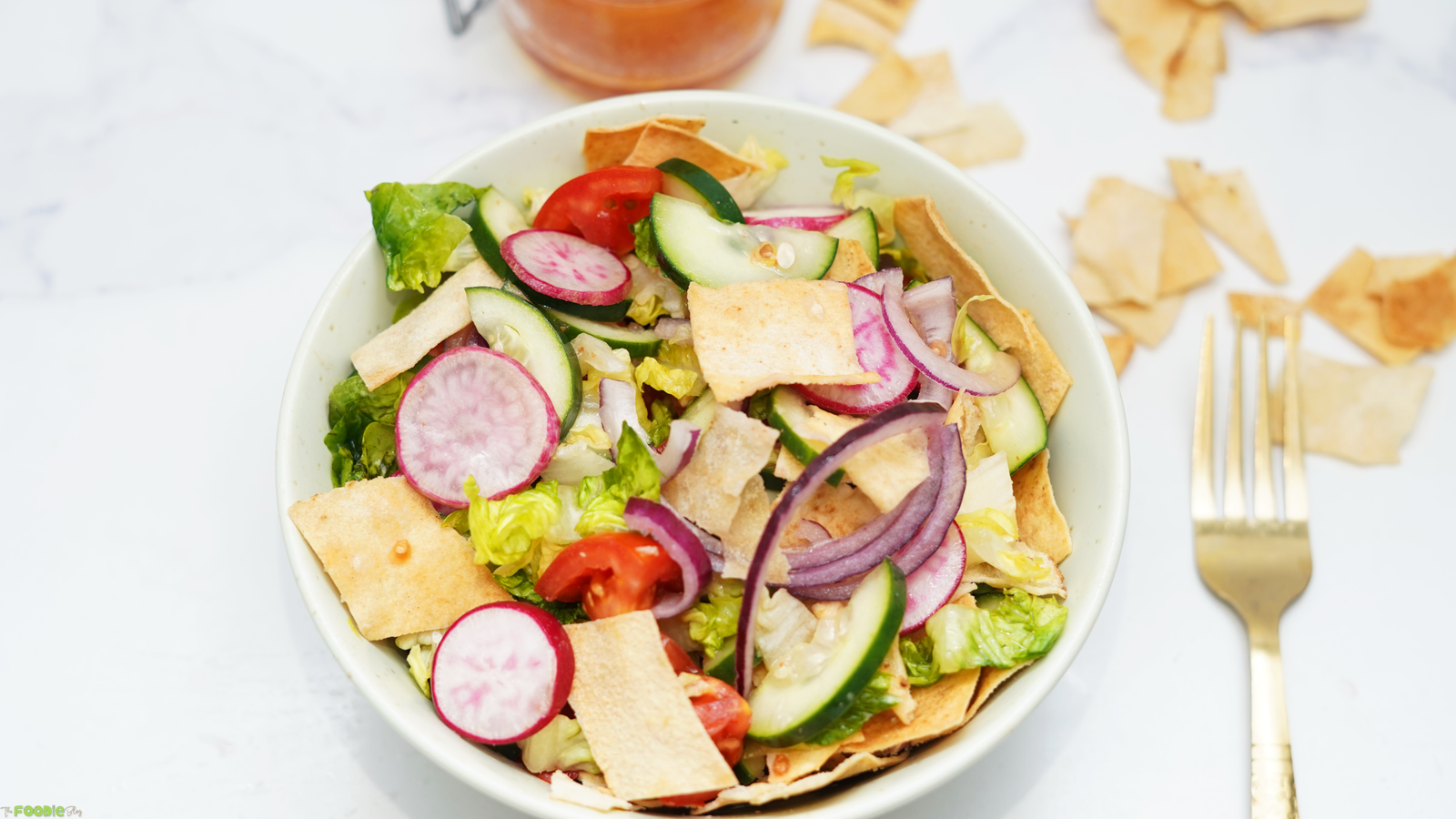 Bowl of Lebanese Fattoush Salad with lettuce, cucumber, tomato, radish, red onion, and crispy pita bread beside a gold fork.