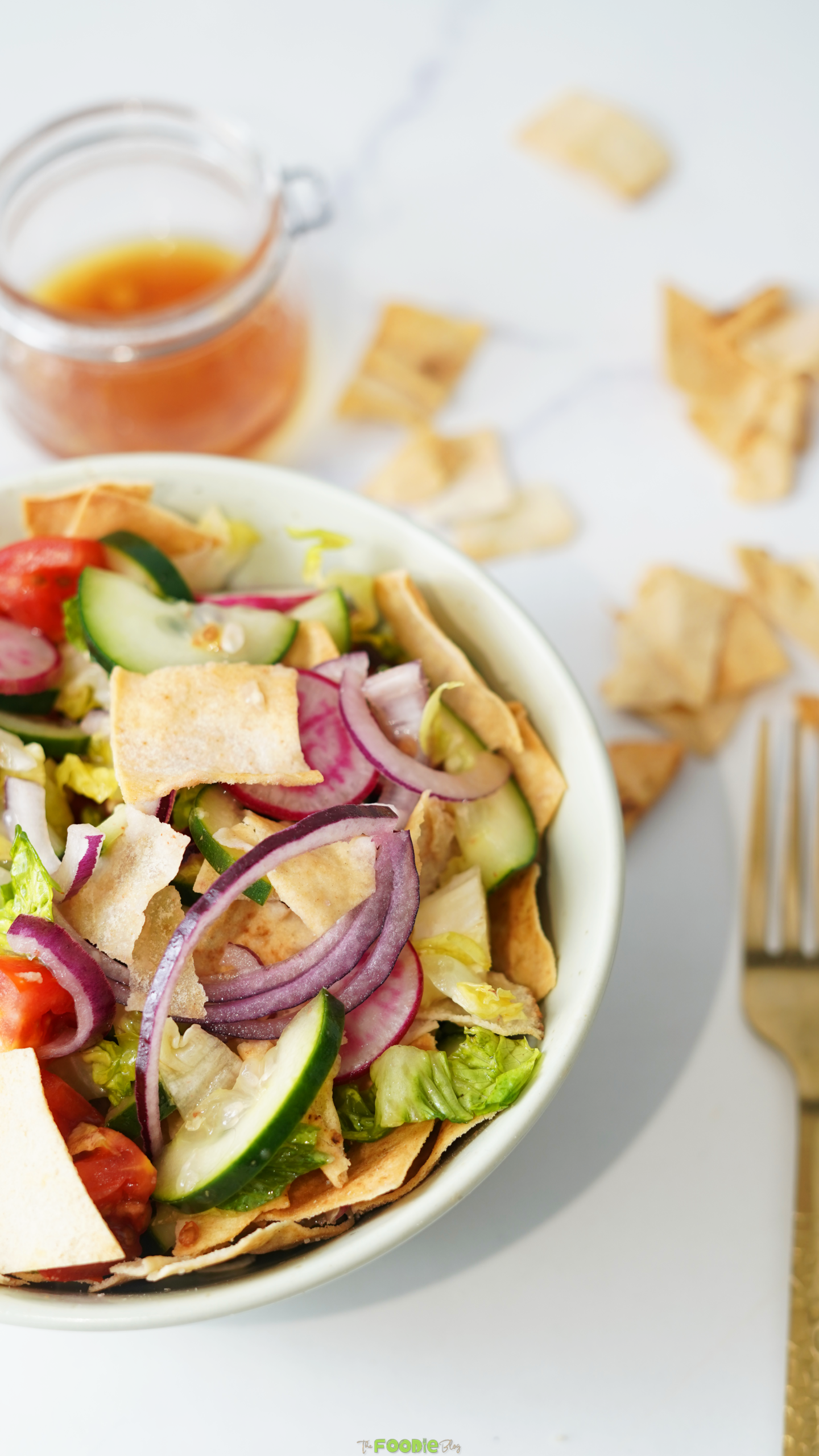 Close-up of Lebanese Fattoush Salad with crispy pita pieces, radish slices, cucumber, lettuce, red onion, and dressing in the background.