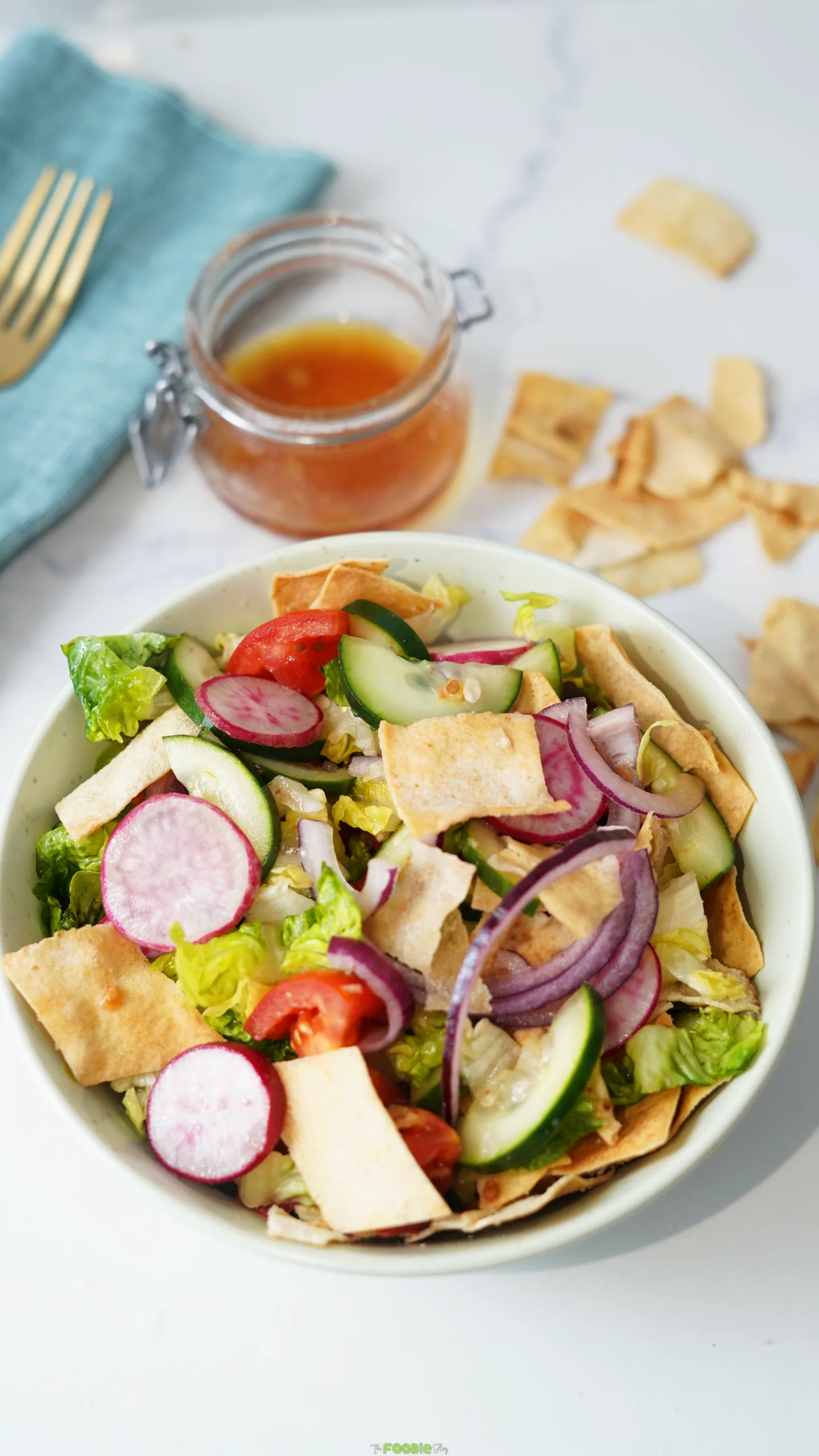 Lebanese Fattoush Salad served in a bowl with cucumbers, tomatoes, radishes, red onion, lettuce, crispy pita, and dressing nearby.